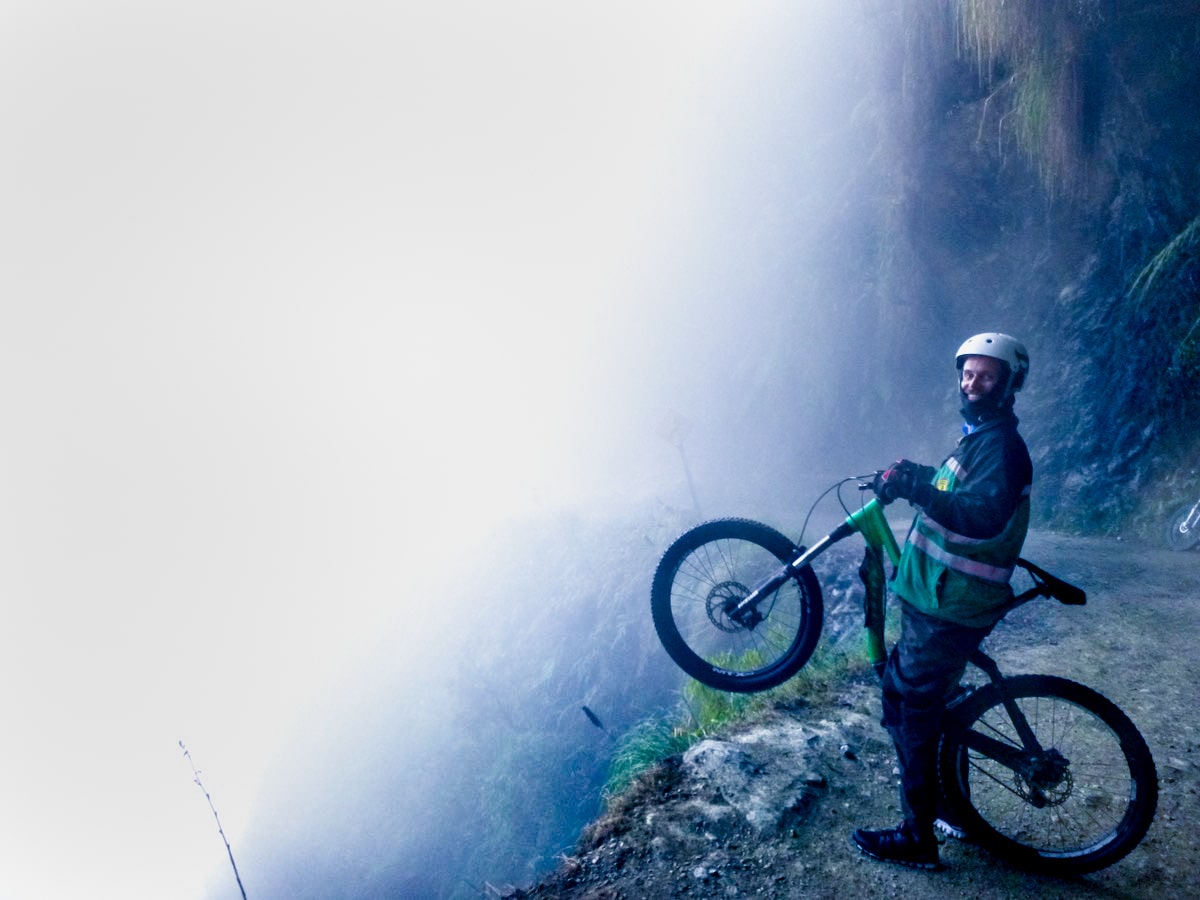 SafetyWing Review (Digital Nomads Insurance & Expats) | cycling bolivias death road A cyclist raises his front wheel over a misty cliff in Yungas Road, Bolivia
