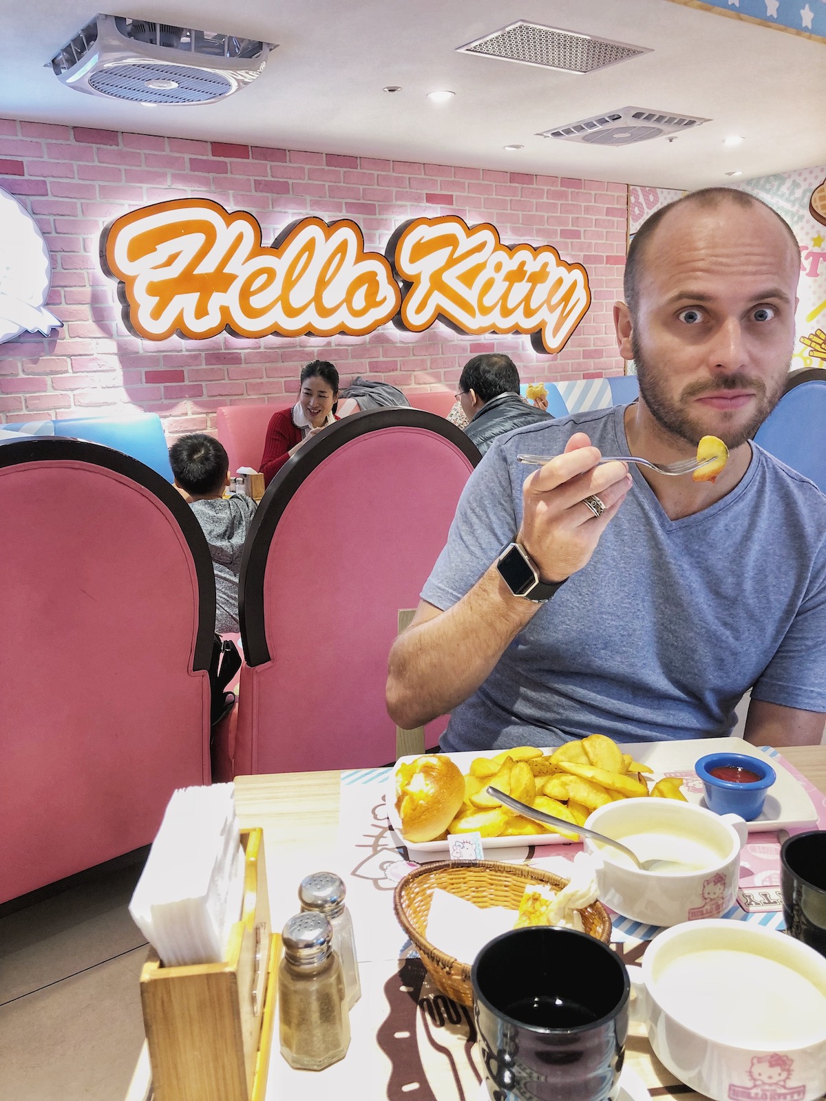 7 Unique & Fun Things To Do in Taipei (Guide For Weirdos!) | Hello Kitty Taiwan A man eats with a funny face in front of a bright Hello Kitty sign
