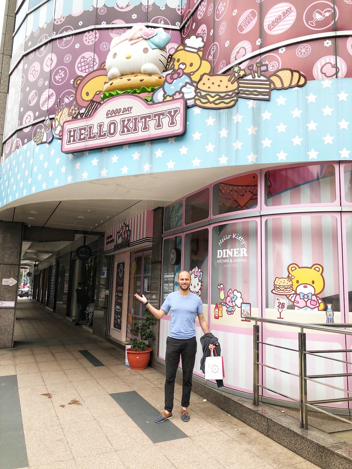 7 Unique & Fun Things To Do in Taipei (Guide For Weirdos!) | Hello kitty Taipei A man in blue smiles and poses outside a pink Hello Kitty restaurant in Taipei, Taiwan