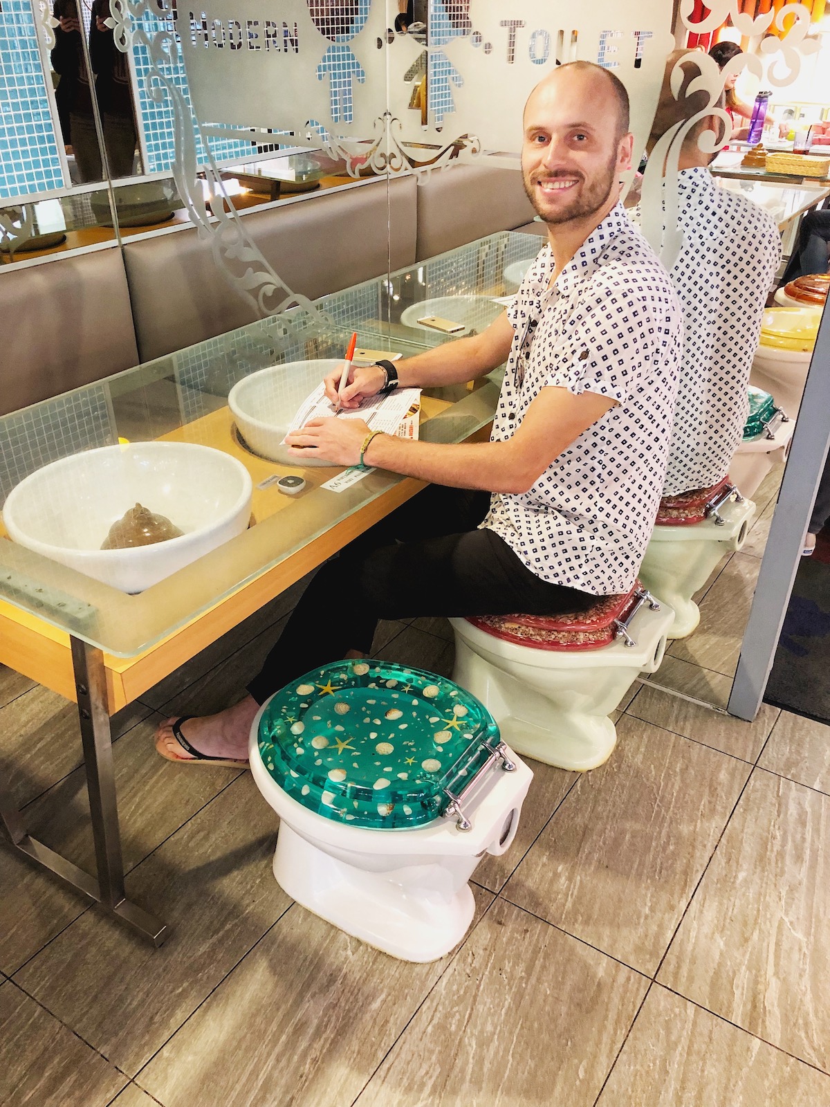 7 Unique & Fun Things To Do in Taipei (Guide For Weirdos!) | Modern Toilet Taiwan A man in a white shirt smiles while writing