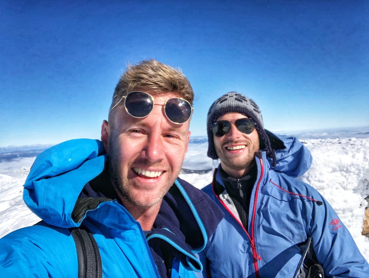 Climbing Mount Kosciuszko in Winter | top of Mount Kosciuszco in winter Two men smile after reaching the top of Australia's tallest mountain