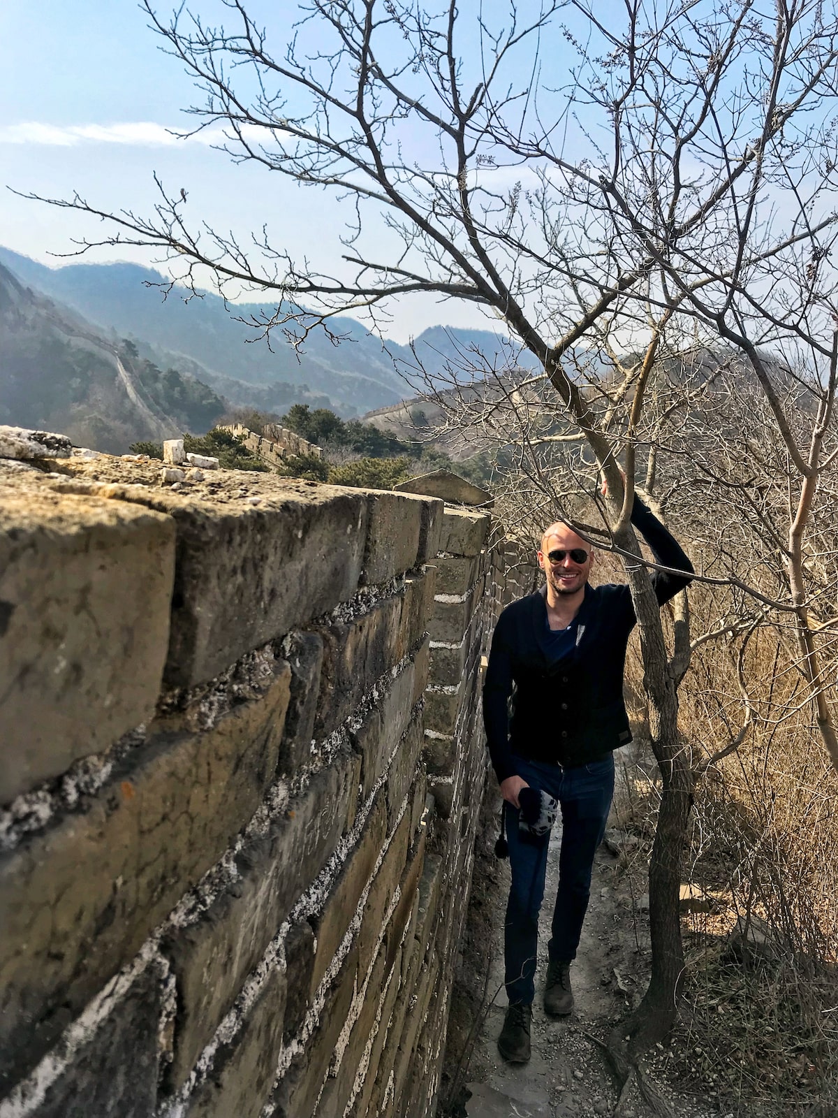 Best Place To See Great Wall of China (No Crowds, No Worries!) | The Wild Great Wall of China best place Male tourist with sunglasses smiles next to a tree in China.