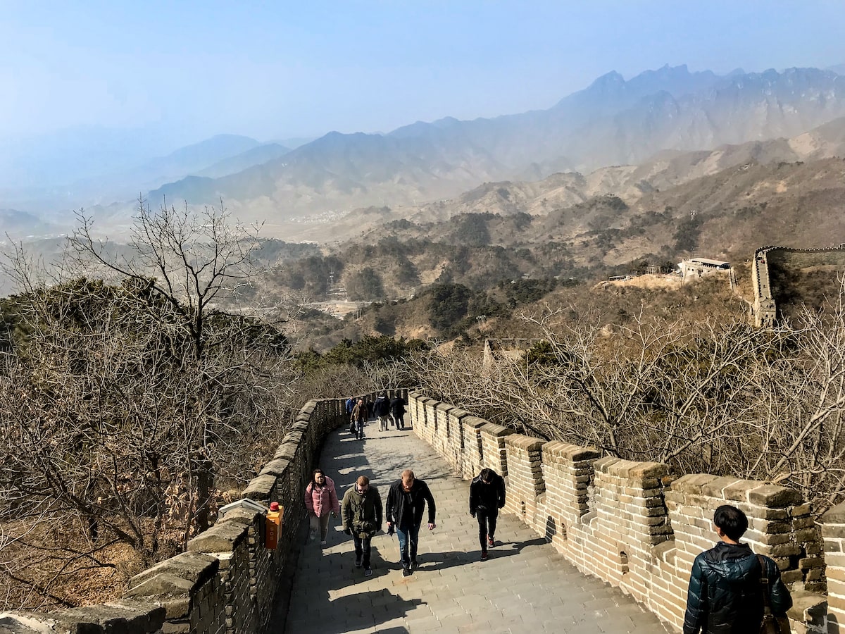 Best Place To See Great Wall of China (No Crowds, No Worries!) | The best place to see the Great Wall of China Tourists walk over a bridge with a mountainous backdrop in Beijing, China.