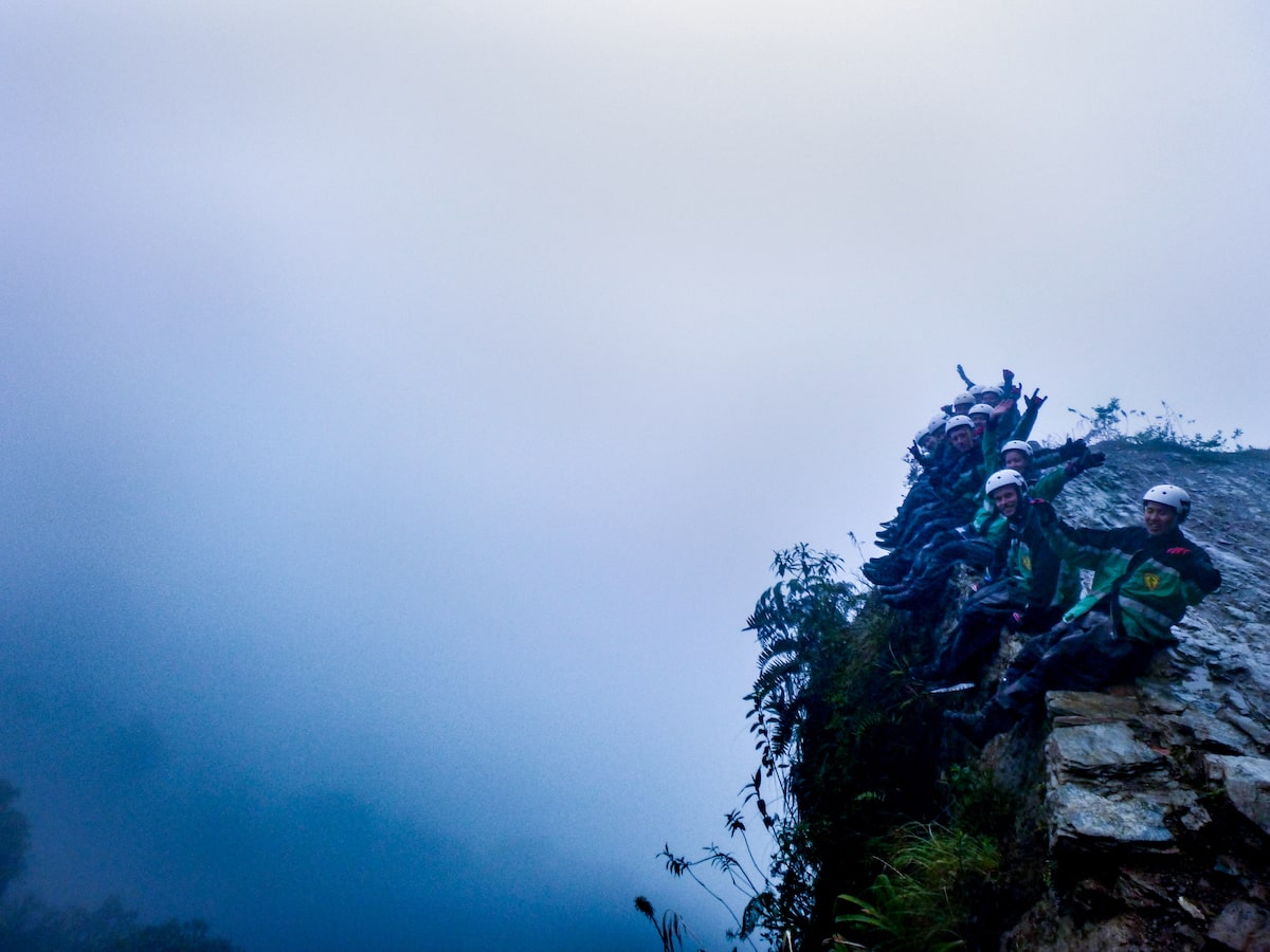 Cycling Down Bolivia's Death Road (How Not To Die!) | death road bolivia cliffs Tourists pose on the edge of the Bolivian Death Road cliff on a foggy day outside of La Paz.