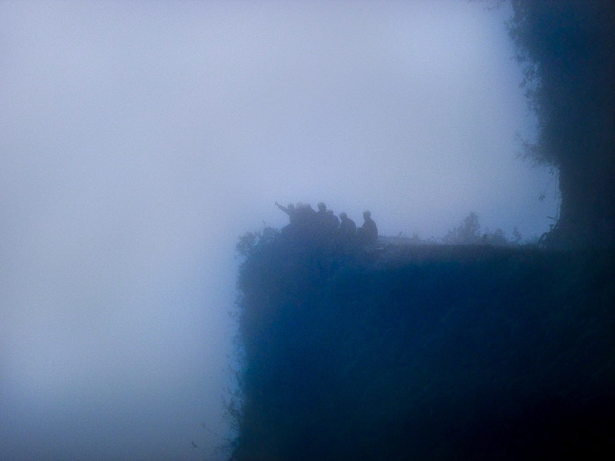 Cycling Down Bolivia's Death Road (How Not To Die!) | foggy death road bolivia People wave in the mist of Bolivia's Death Road while sitting on a cliff.