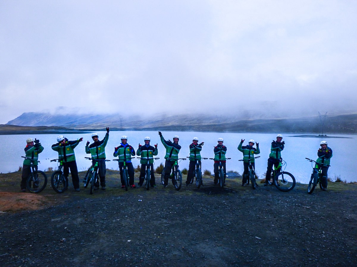 Cycling Down Bolivia's Death Road (How Not To Die!) | tour bolivia death road A team of cyclists pose with arms in the air at the start of Bolivia's Death Road.