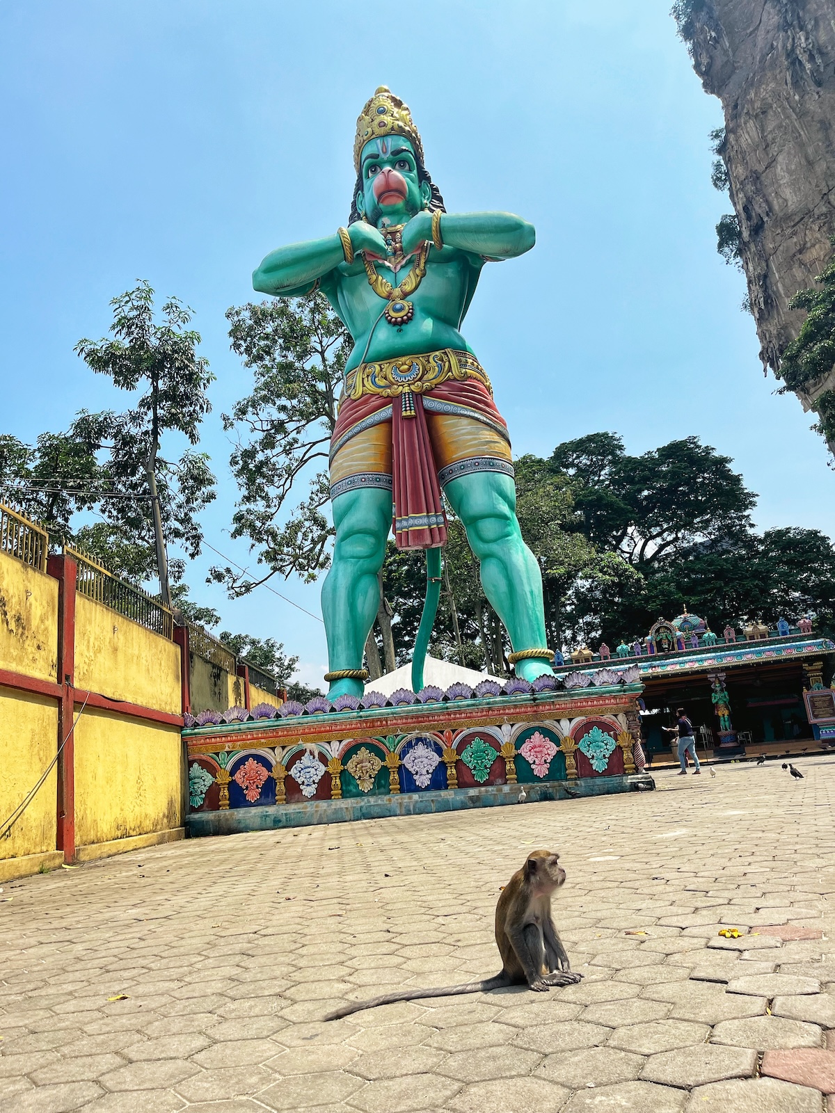 How Many Days Should You Spend in Kuala Lumpur? | 3 day Kuala Lumpur intinerary A small monkey looks onward below a giant statue of a Hindu monkey God in Kuala Lumpur