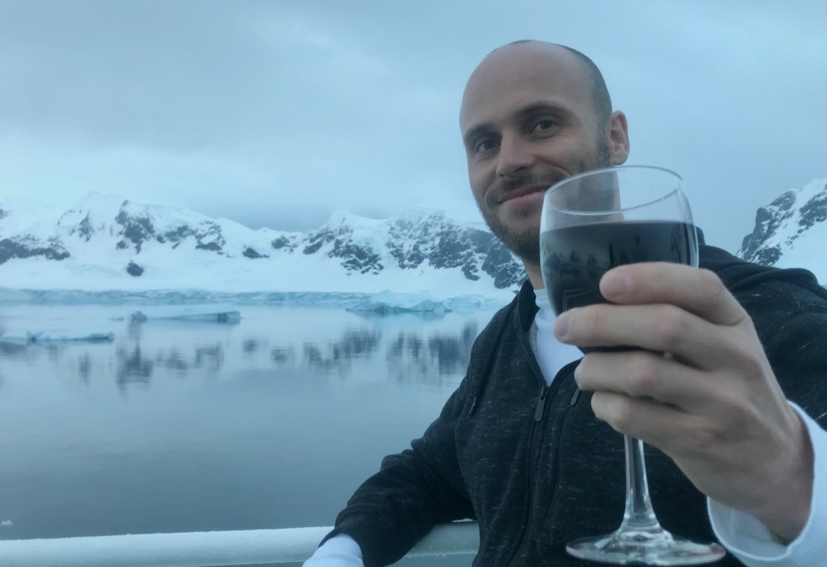 23 Best Things To Do in Ushuaia, Argentina | Antarctica tourist A man raises a glass of red wine near a glacier which reflects off a body of water