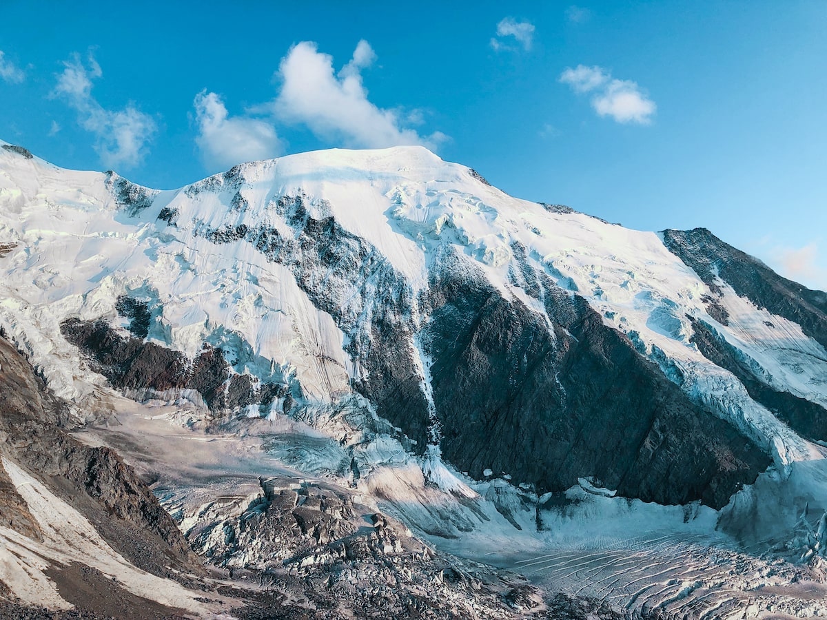 Mont Blanc Climb (The Beginner's Guide To Summiting in 2024) | Base camp Mont Blanc A snow-capped black mountain on a bright blue-skyed day.