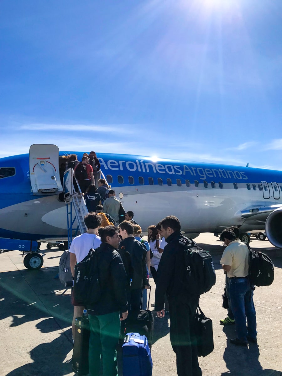 The Ultimate Guide To Visiting Both Sides of Iguazu Falls | Buenos Aries Airport People queue up to get on blue and white an Aerolineas Argentinas plane
