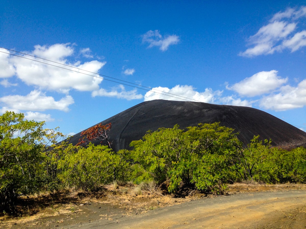 Volcano in Boarding in Leon, Nicaragua (Cerro Negro) | Cerro Negro A volcano on a clear blue sky day with green trees outside of it.