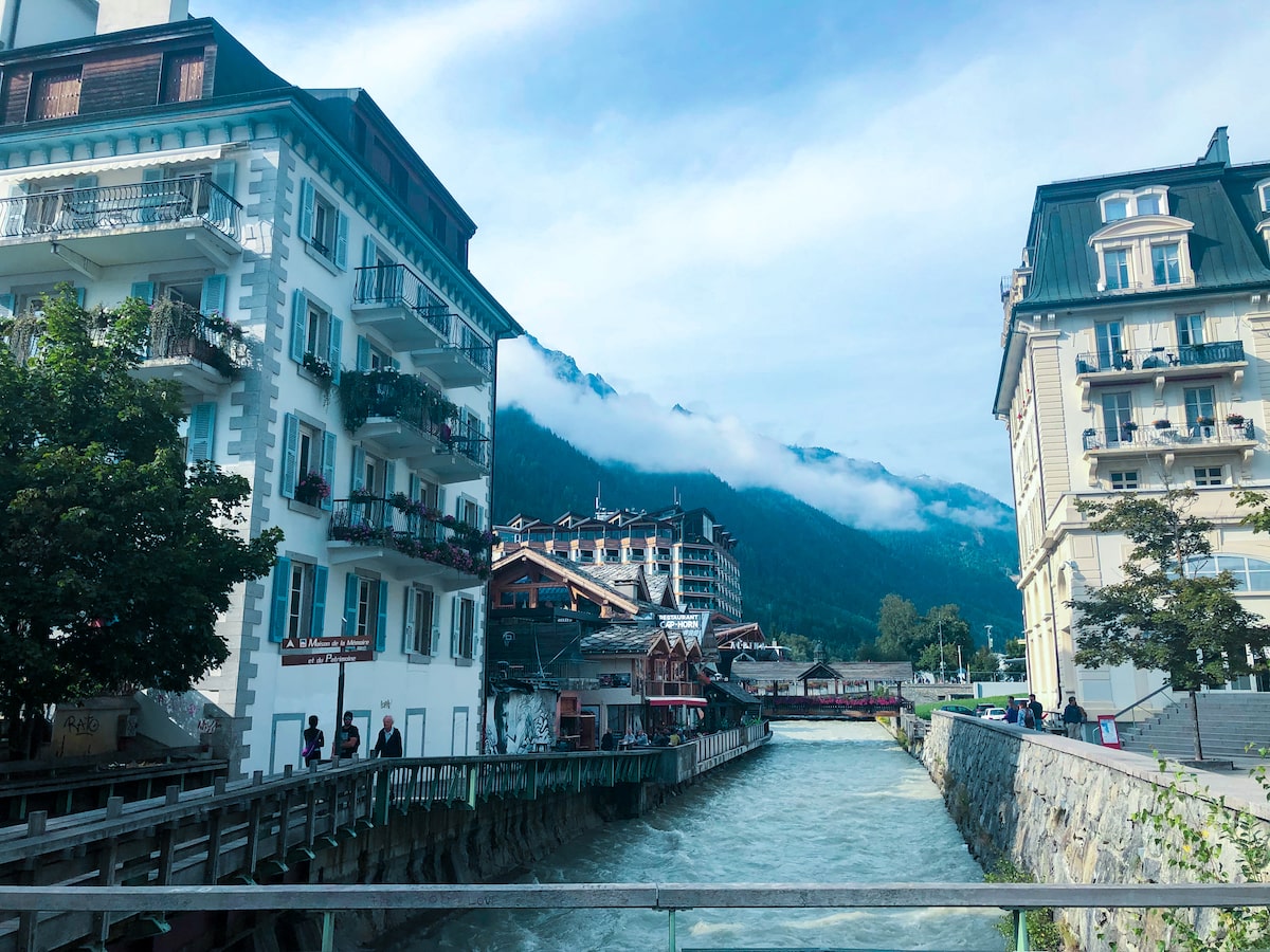 Mont Blanc Climb (The Beginner's Guide To Summiting in 2024) | Chamonix base Mont Blanc A bed of water flows through a pretty citym misty clouds drift over nearby mountains,