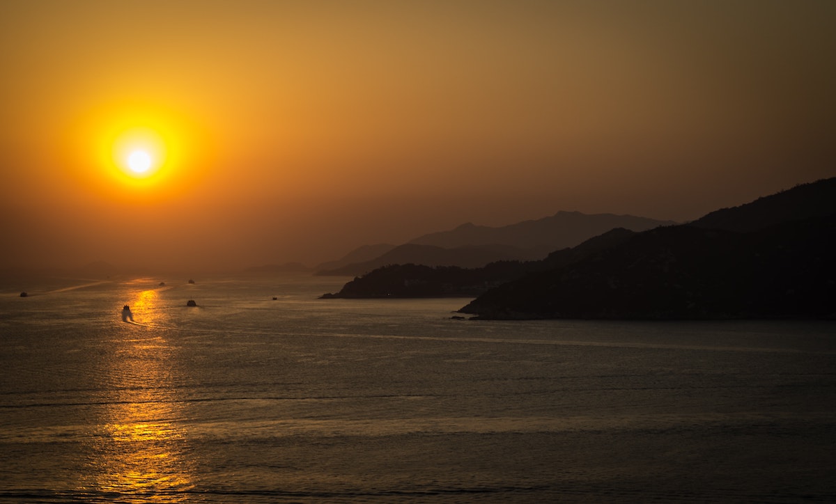 The Ultimate Hong Kong Bucket List: 25 Best Things To Do! | Cheung Chau island Boats riding on the sea at sunset near hilly mountains at Cheung Chau Island, Hong Kong