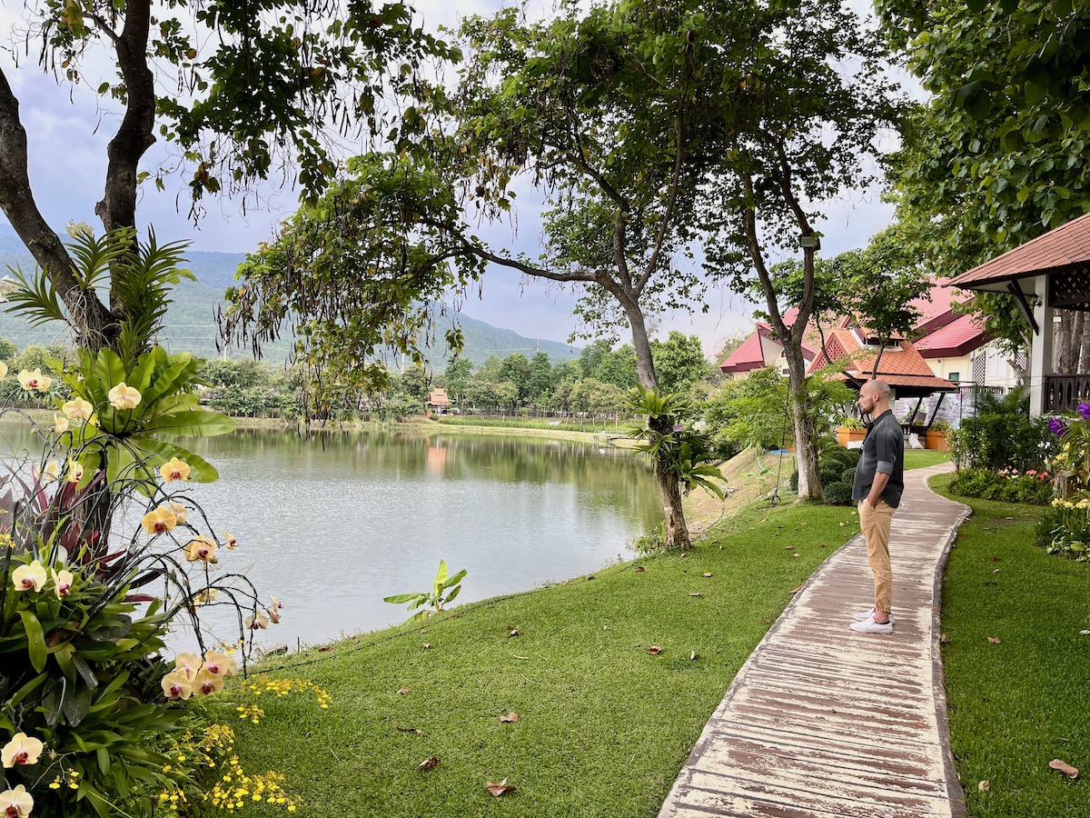 Detailed Chiang Mai Digital Nomad Guide For 2024 | Chiang Mai pretty cafe A man in a black shirt looks out into a beautiful view of a lake and trees surrounding a green mountain in Chiang Mai, Thailand