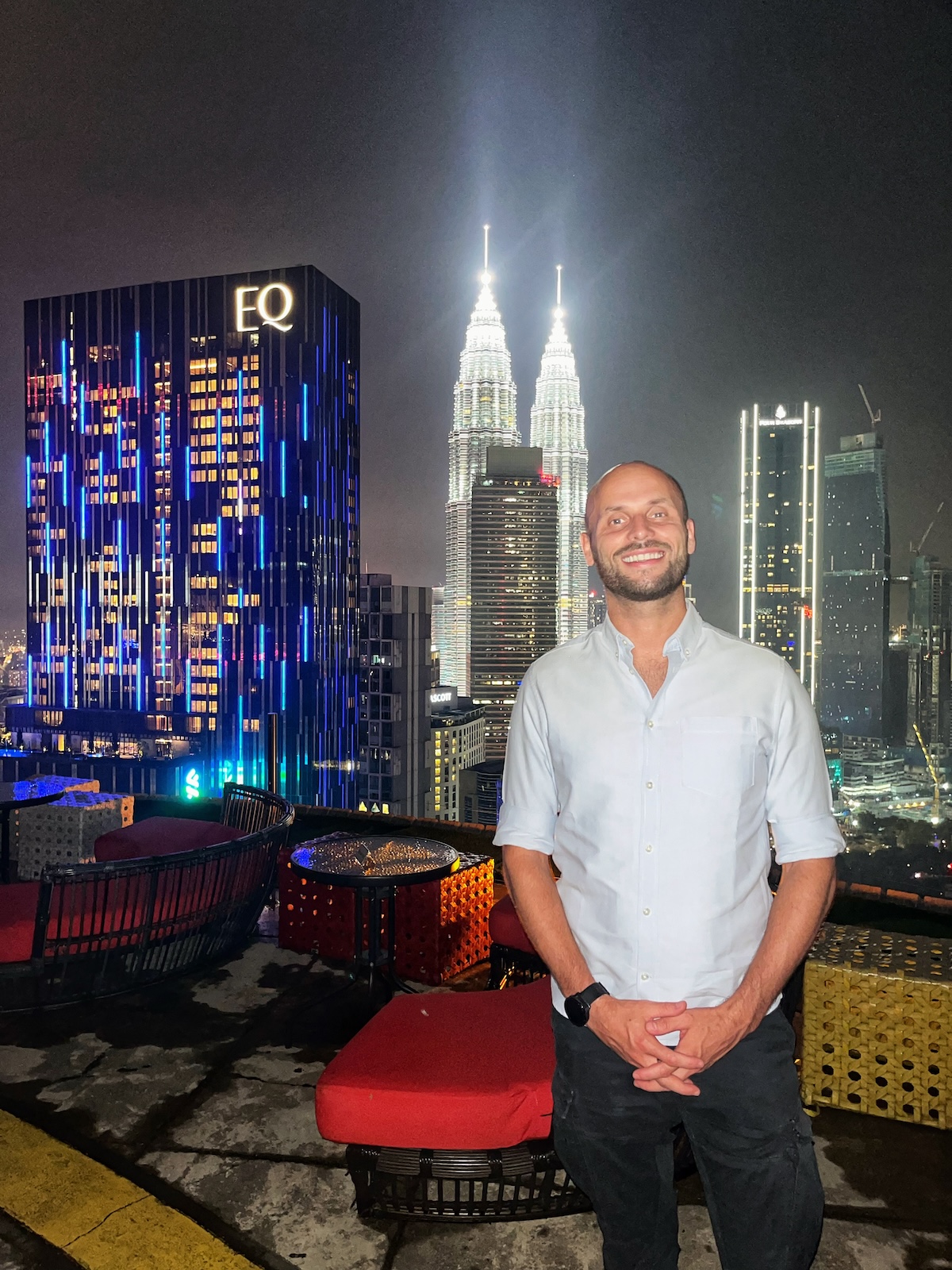 How Many Days Should You Spend in Kuala Lumpur? | Helibar Kuala Lumpur A man standing on the rooftop of Helibar in Kuala Lumpur at night, with the illuminated Petronas Twin Towers and other skyscrapers in the background. The vibrant city lights create a stunning urban skyline.