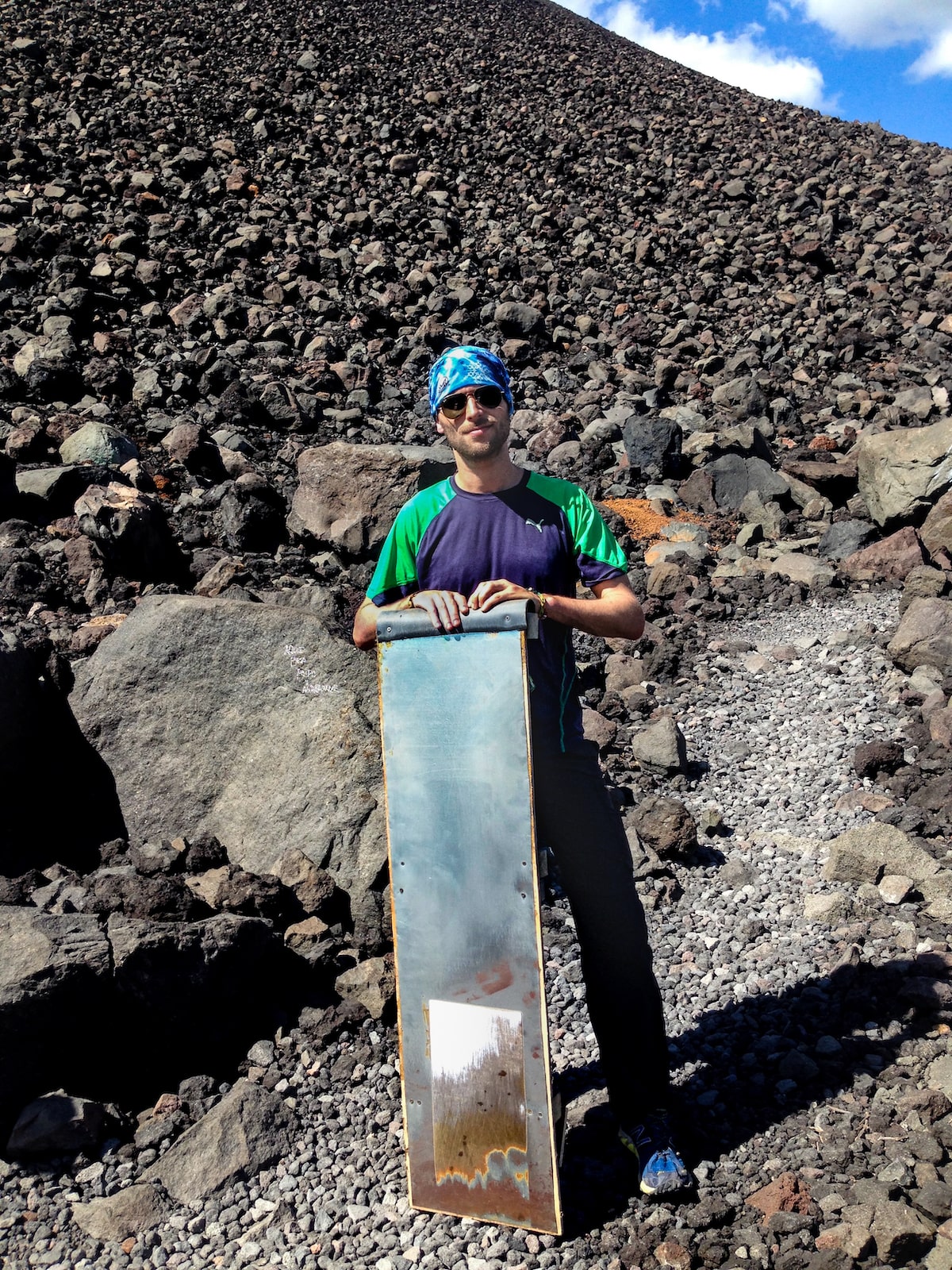 Volcano in Boarding in Leon, Nicaragua (Cerro Negro) | Hiking Cerro Negro A male tourist in sunglasses and a blue bandana poses with a volcano board at the bottom of Cerro Negro, Nicaragua.