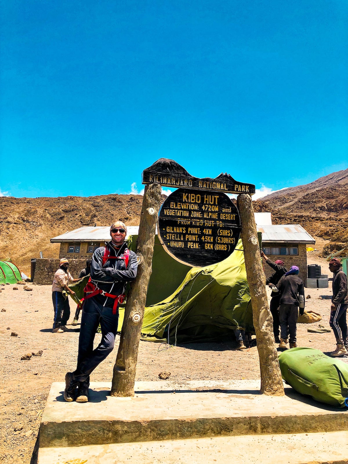 The Beginner's Guide To Climbing Mount Kilimanjaro | Kibo Hut climbing Kilimanjaro A male hiker confidently leans against a signpost in Kilimanjaro National Park.