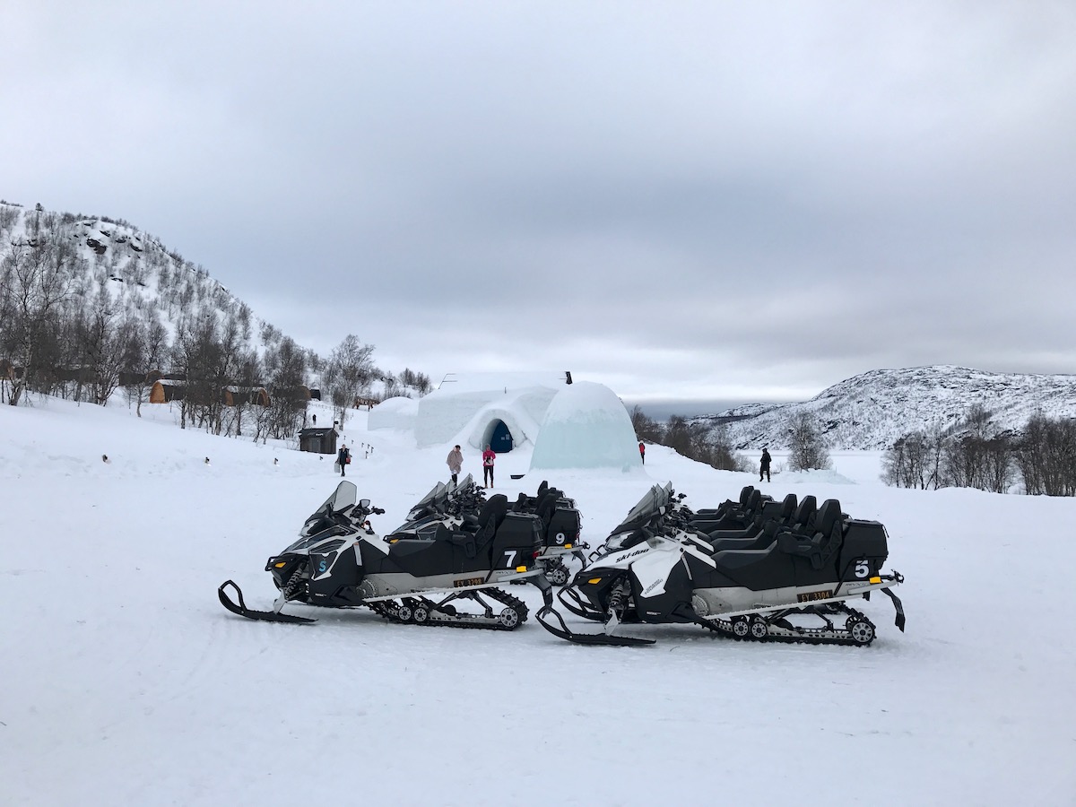 Staying in The Kirkenes Snow Hotel in Norway (Bucket List!) | Kirkenes Snow Hotel Norway An igloo and snow hotel surrounded by snowy mountains with snowmobiles parked in front