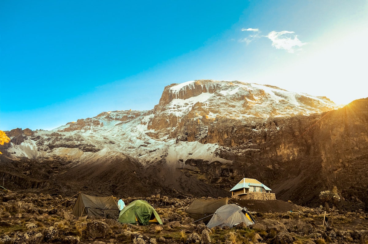 The Beginner's Guide To Climbing Mount Kilimanjaro | Lemosho Route Kilimanjaro An icy mountain with tents and a hut during the day on Mount Kilimanjaro, Tanzania.