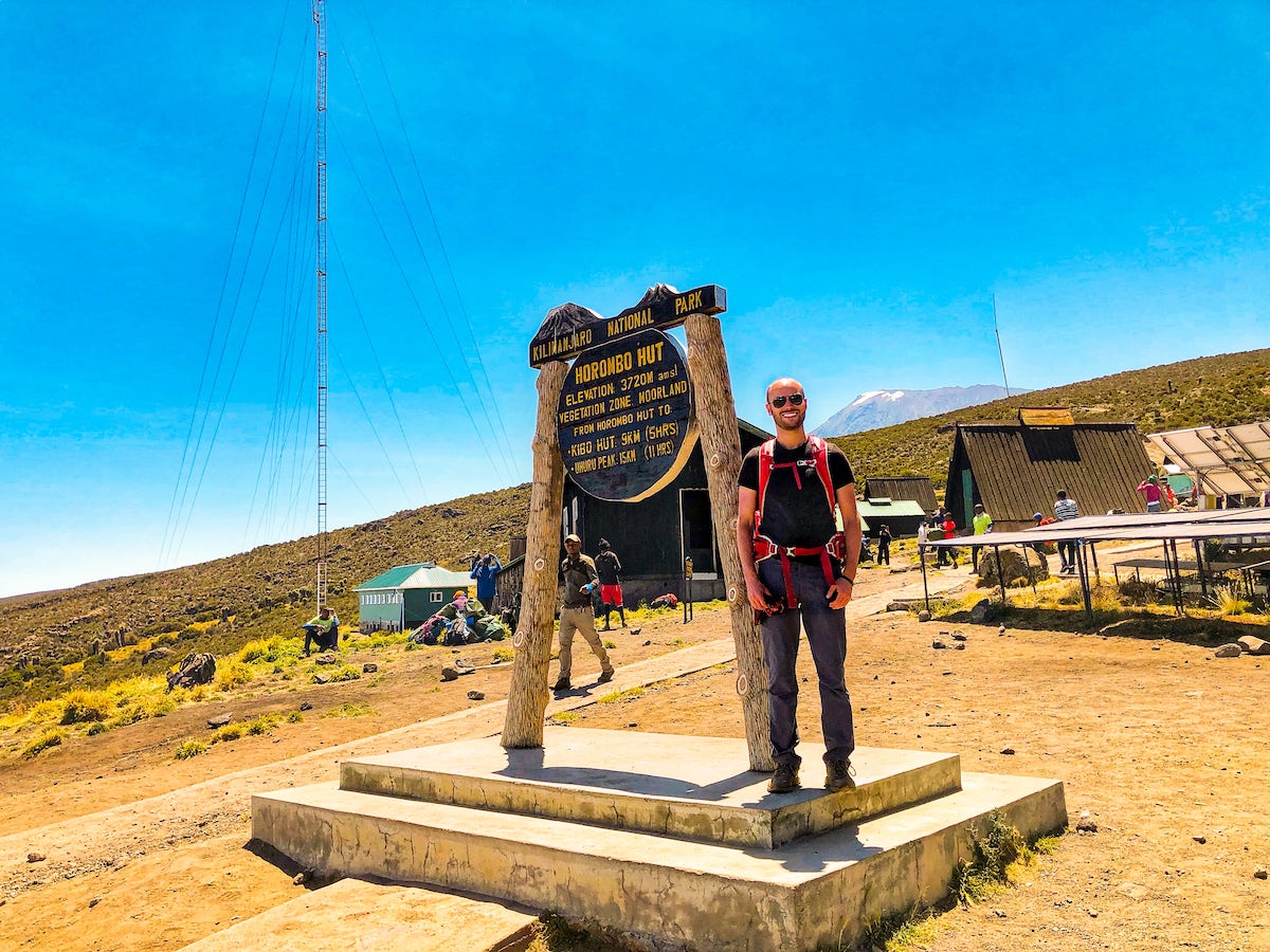 The Beginner's Guide To Climbing Mount Kilimanjaro | Marangu Route huts Tourist at a sign reading "Horombo Hut."