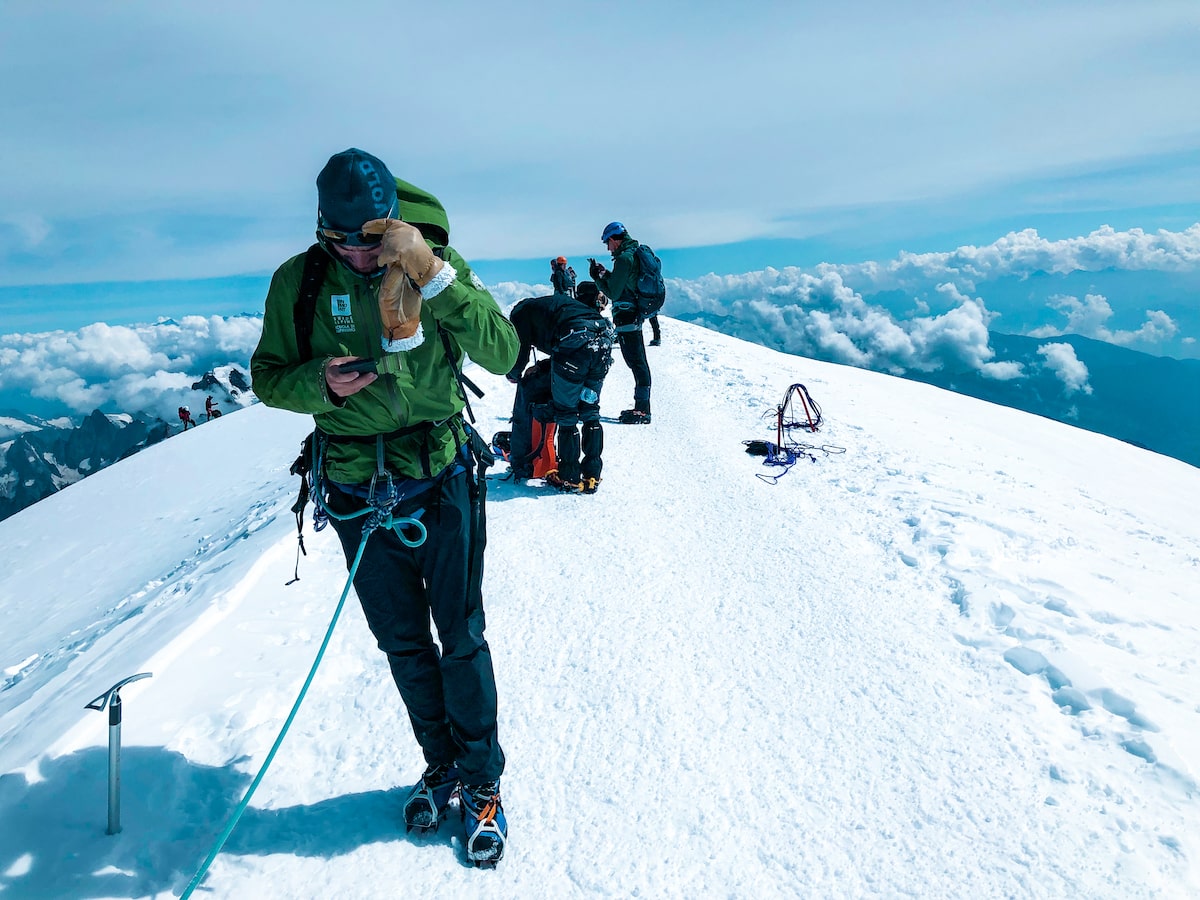 Mont Blanc Climb (The Beginner's Guide To Summiting in 2024) | On top of Mont Blanc A mountain guide plays on his phone on the top of Mont Blanc's snowy summit.