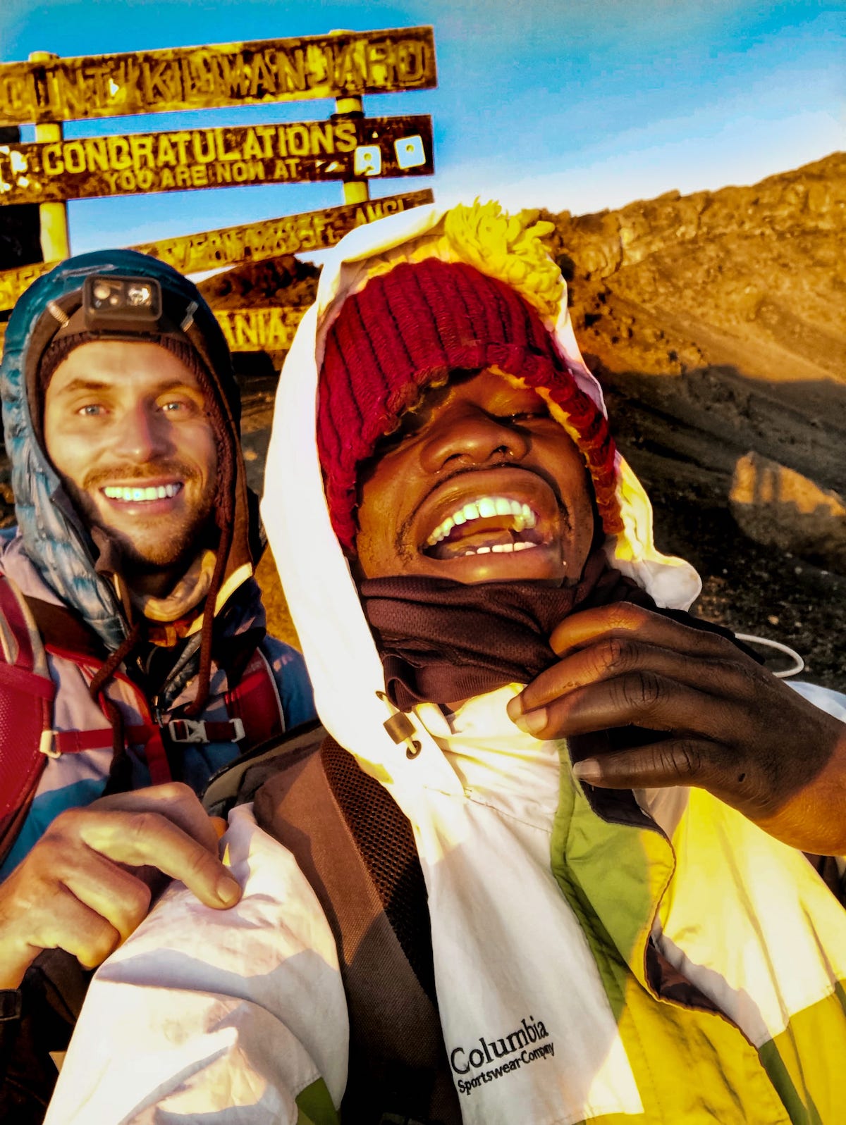 The Beginner's Guide To Climbing Mount Kilimanjaro | On way down from Kilimanjaro Two men smile with mountain gear on.
