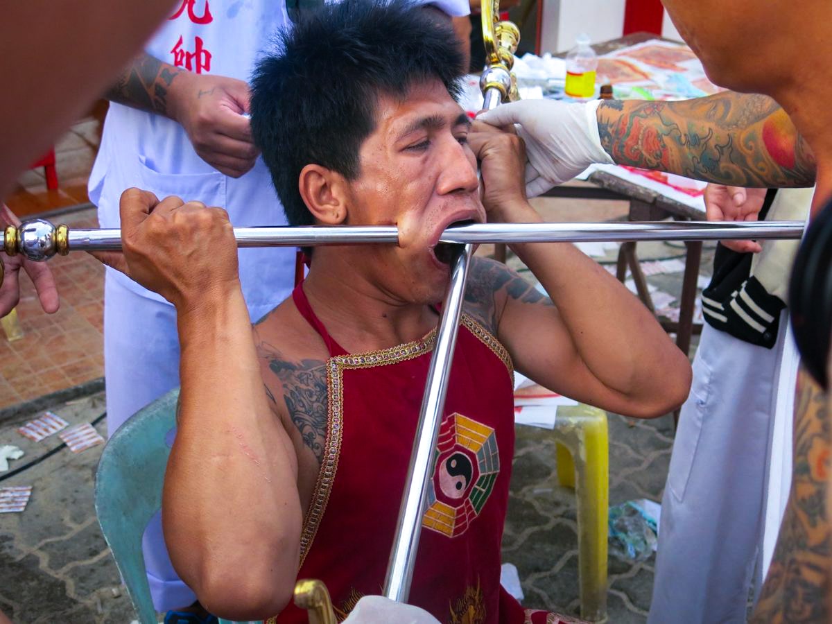 17 Best Thailand Festivals (That You May Never Heard Of) | Phuket Vegetarian Festival An Asian man with two large metal poles impaled through his face at the Phuket Thailand Festival