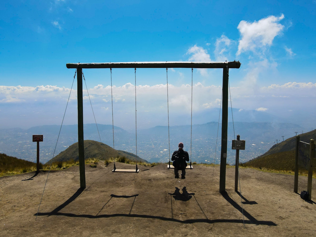 One Week in Quito, Ecuador: 23 Things in 7 Days! | Pichincha volcano swing A tourist sits on a giant swing facing a mountainous city centre.