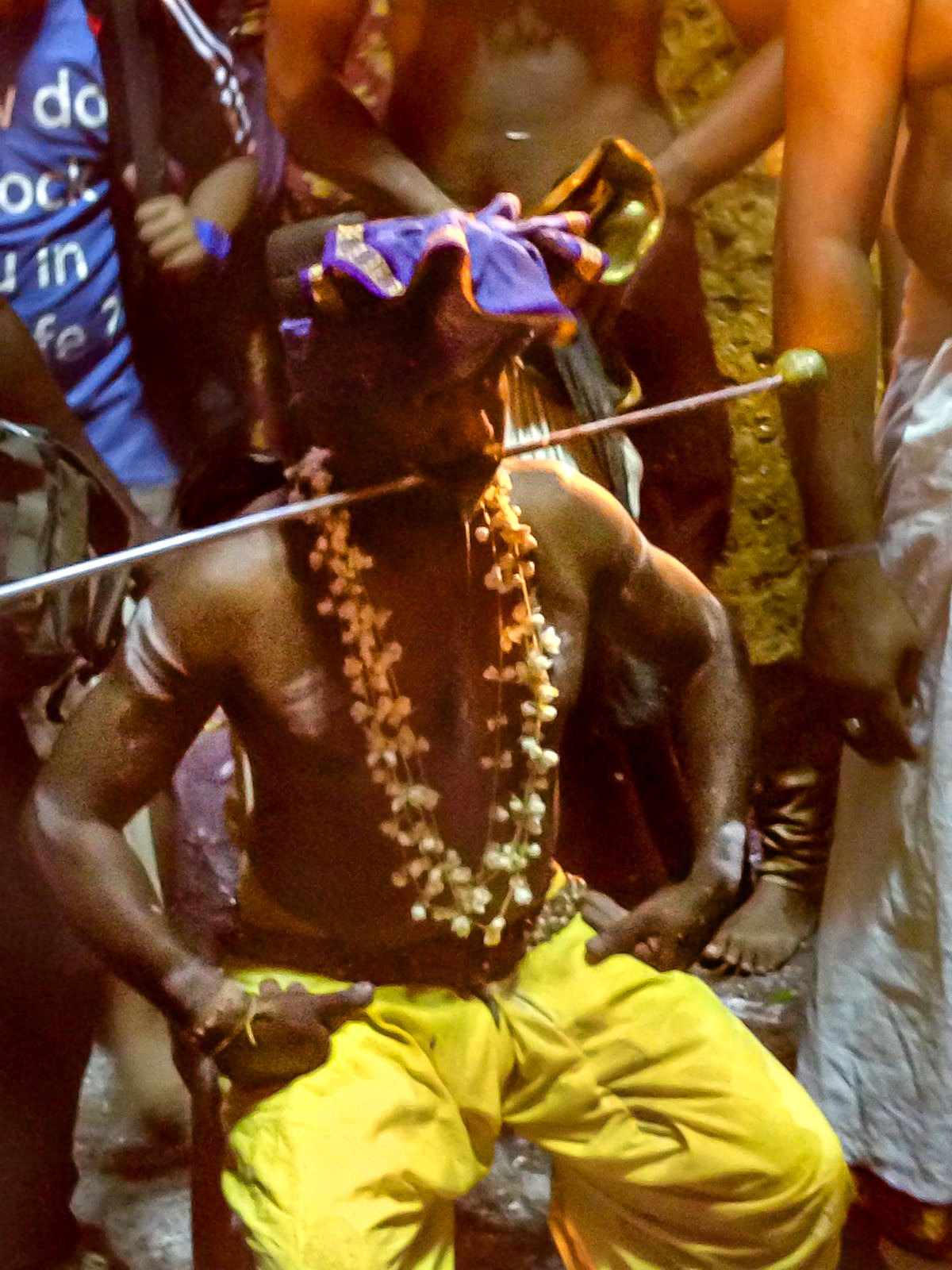 Thaipusam Festival at Batu Caves in Kuala Lumpur 2025 | Pierced Hindu Thaipusam in Batu Caves A Hindu man in yellow trousers sits with a metal pole through his cheeks at the Thaipusam Festival in Batu Caves, just outside of Malaysia's capital city.