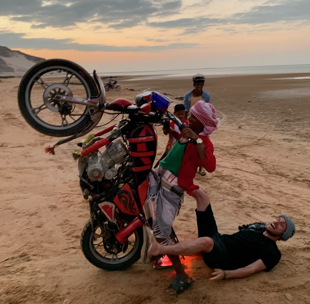SafetyWing Review (Digital Nomads Insurance & Expats) | Socotra Island motorbike beach A tourist laughs as he falls off a young man's motorbike in Socotra Island, Yemen