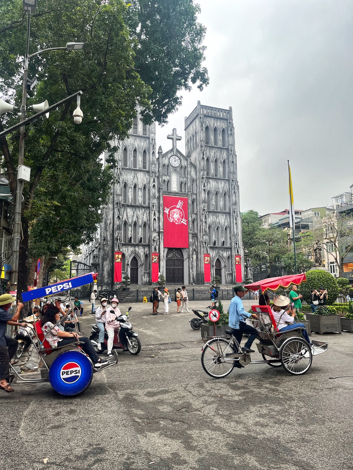 One Day in Hanoi Itinerary: No Transport Needed (Walking Only!) | St Josephs Cathedral Hanoi A grey gothic building with red decorations in front of busy traffic in central Hanoi, Vietnam