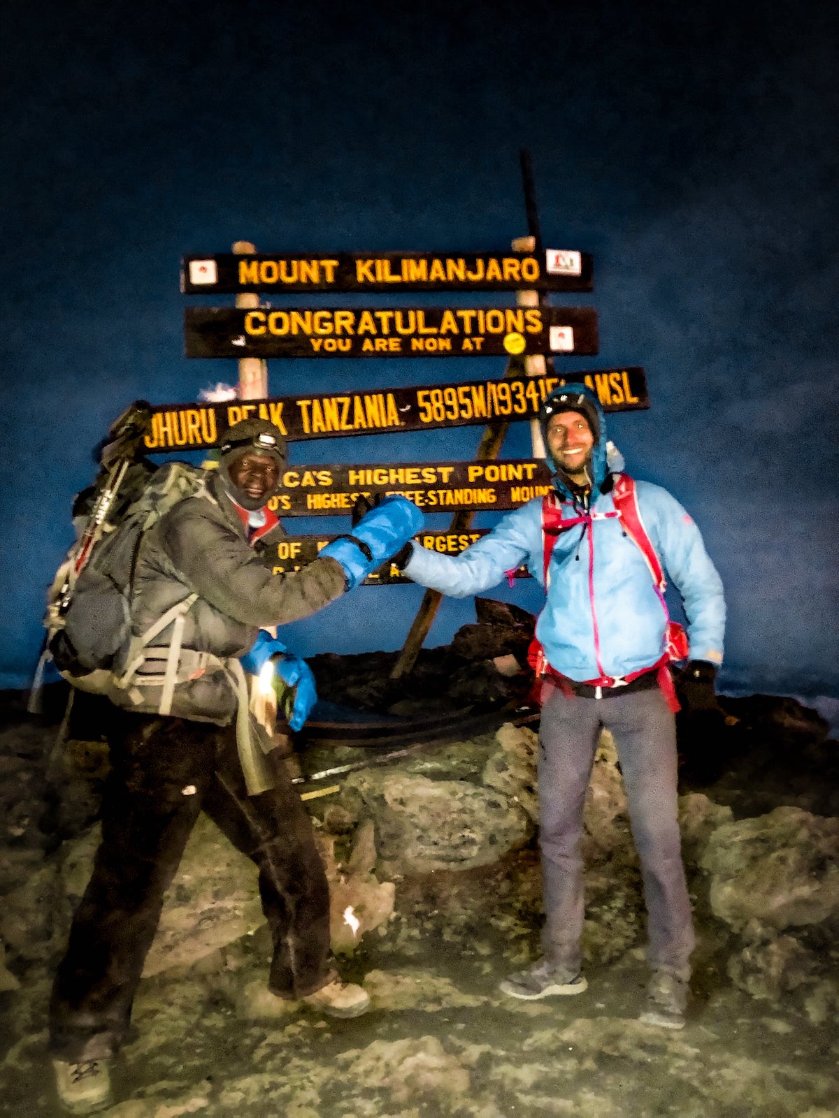 The Beginner's Guide To Climbing Mount Kilimanjaro | Summiting Kilimanjaro Two men shake hands on the summit of Mount Kilimanjaro in Tanzania, East Africa.