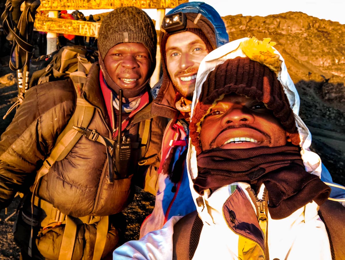The Beginner's Guide To Climbing Mount Kilimanjaro | Team Kilimanjaro Three men smile with mountain gear on.