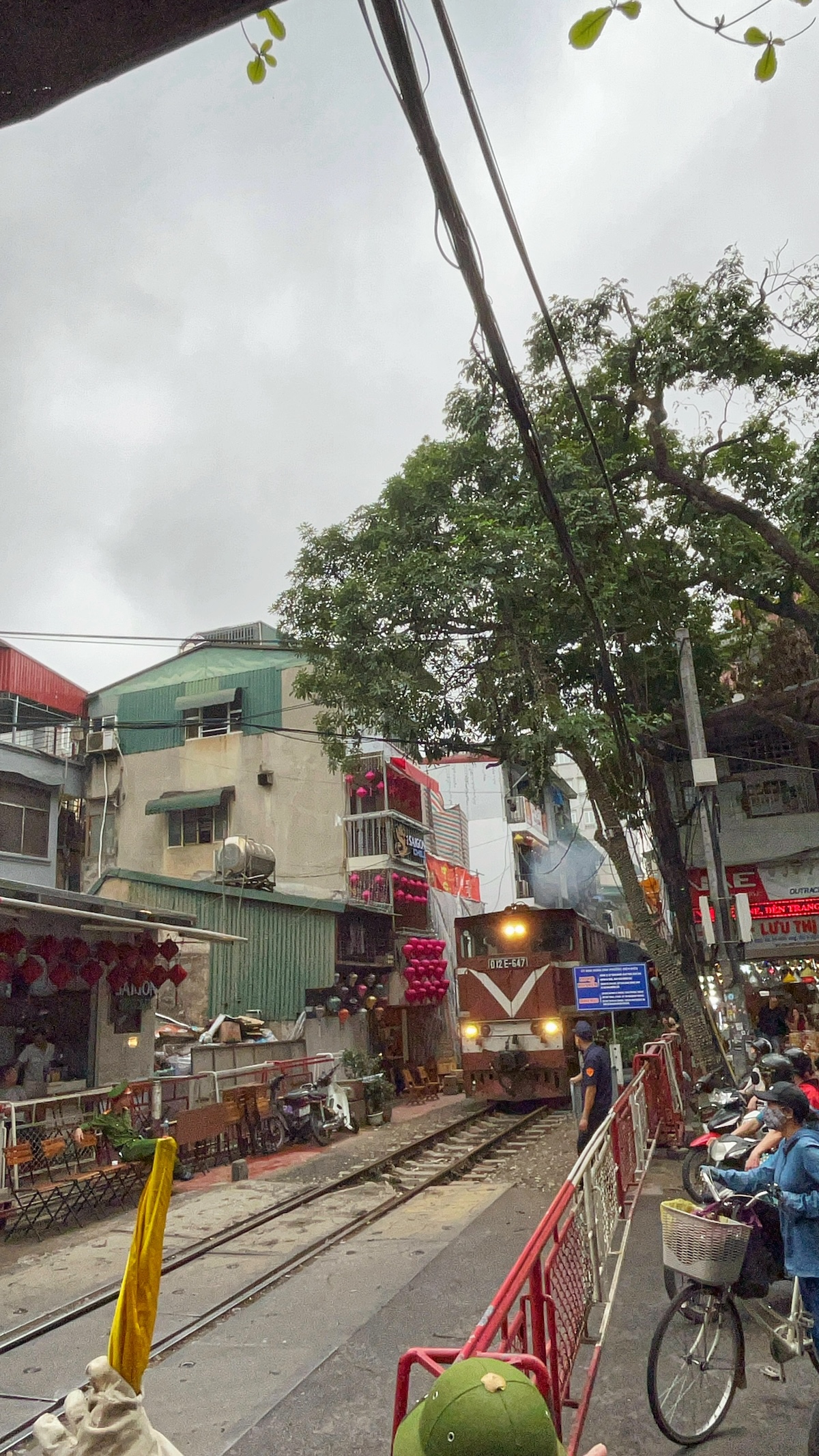 One Day in Hanoi Itinerary: No Transport Needed (Walking Only!) | Train moving Hanoi Train Street Locals wait behind a barrier while a train steals through Hanoi Train Street in Vietnam
