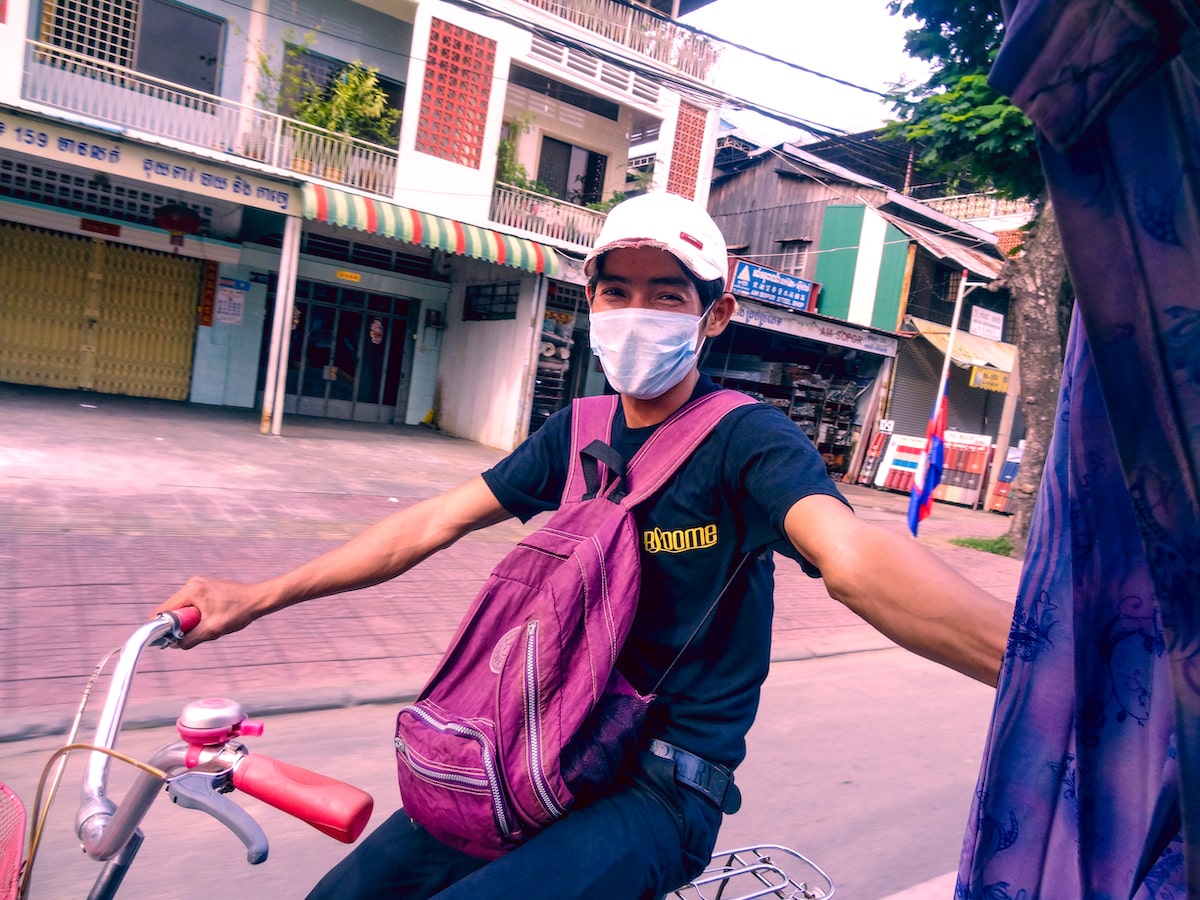 The Rise and Fall of The Khmer Rouge Regime in Cambodia | Transport in Phnom Penh A man smiles in a pollution mask as he holds onto a tuk-tuk in Phnom Penh, Cambodia