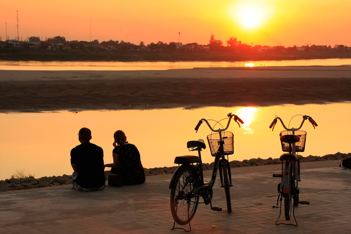 15 Things To Do in Vientiane, Laos (Includes Day Trips) | Vientiane cycling Silhouetted couple watching the sunset at Mekong river waterfront, Vientiane, Laos