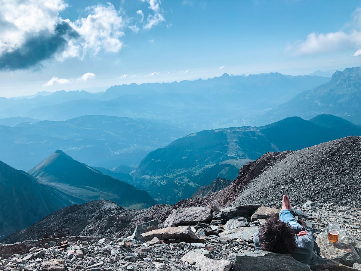 Mont Blanc Climb (The Beginner's Guide To Summiting in 2024) | Views from Mont Blanc A man sits with a beer, overlooking a mountainous region in Mont Blanc, France.
