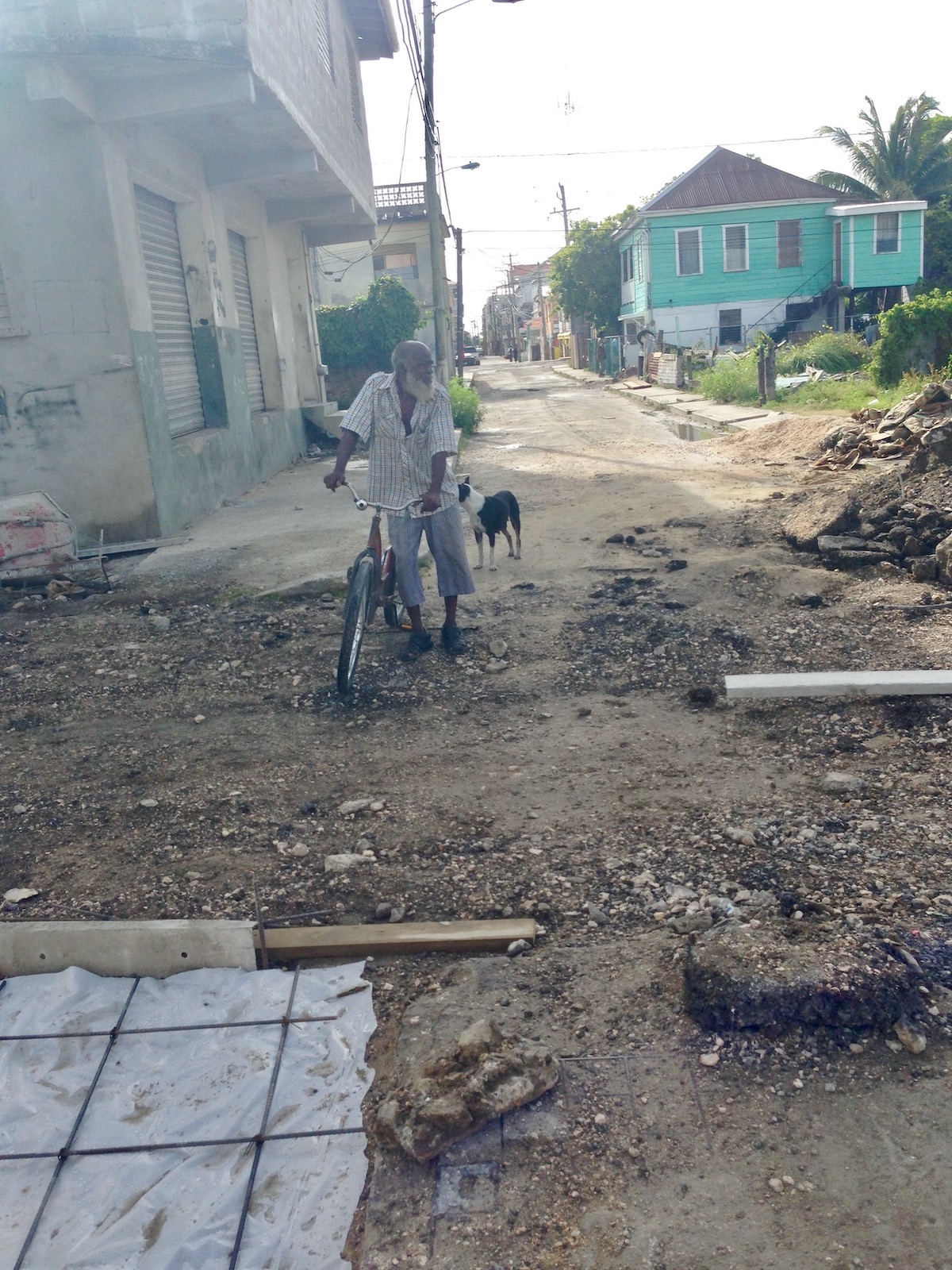 How To Cross The Mexico-Belize Border in 2024 | belize city An old man with a long white beard walks with his dog and a bike in a gritty neighbourhood.