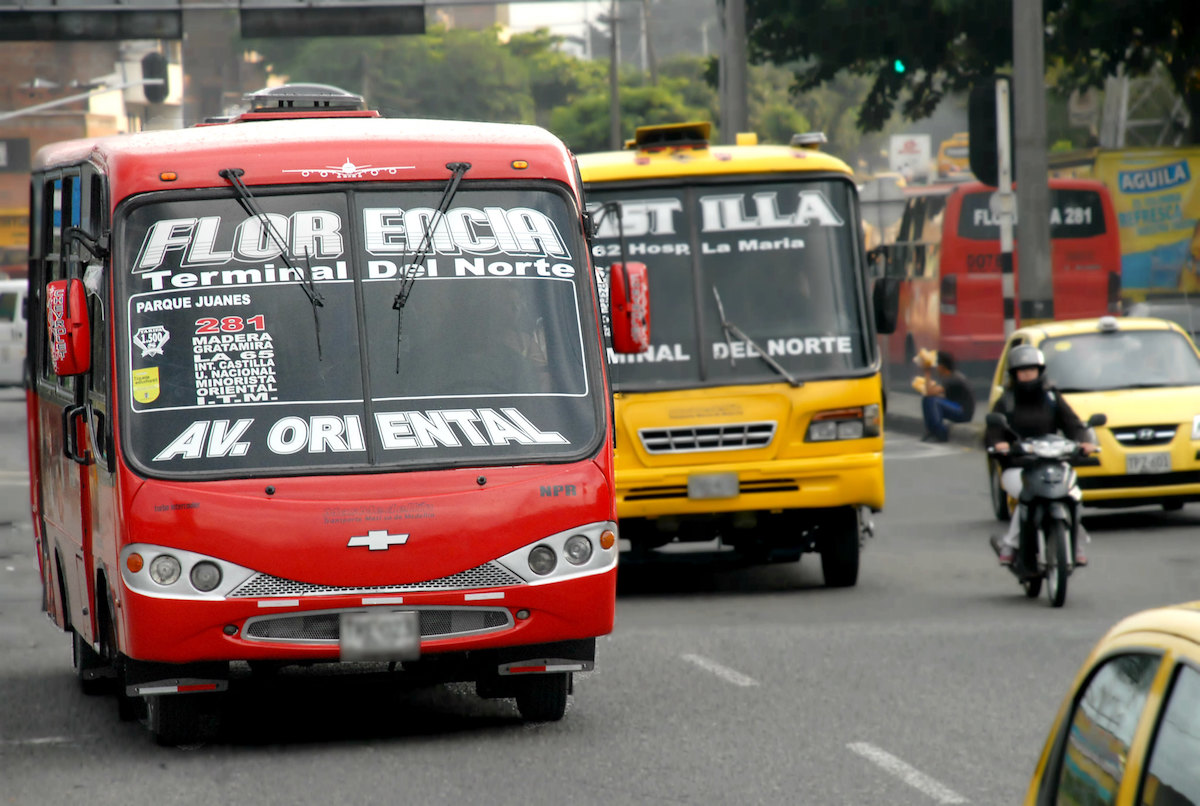 Public Transport in Medellin, Colombia: How To Get Around | bus medellin A red bus and yellow bus drive alongside a motorbike in Medellin, Colombia.