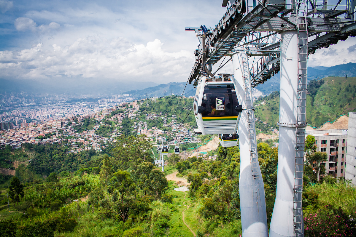 Public Transport in Medellin, Colombia: How To Get Around | cable car medellin A cable car moves as it overlooks green trees, mountains and the city centre on a sunny day in Medellin.