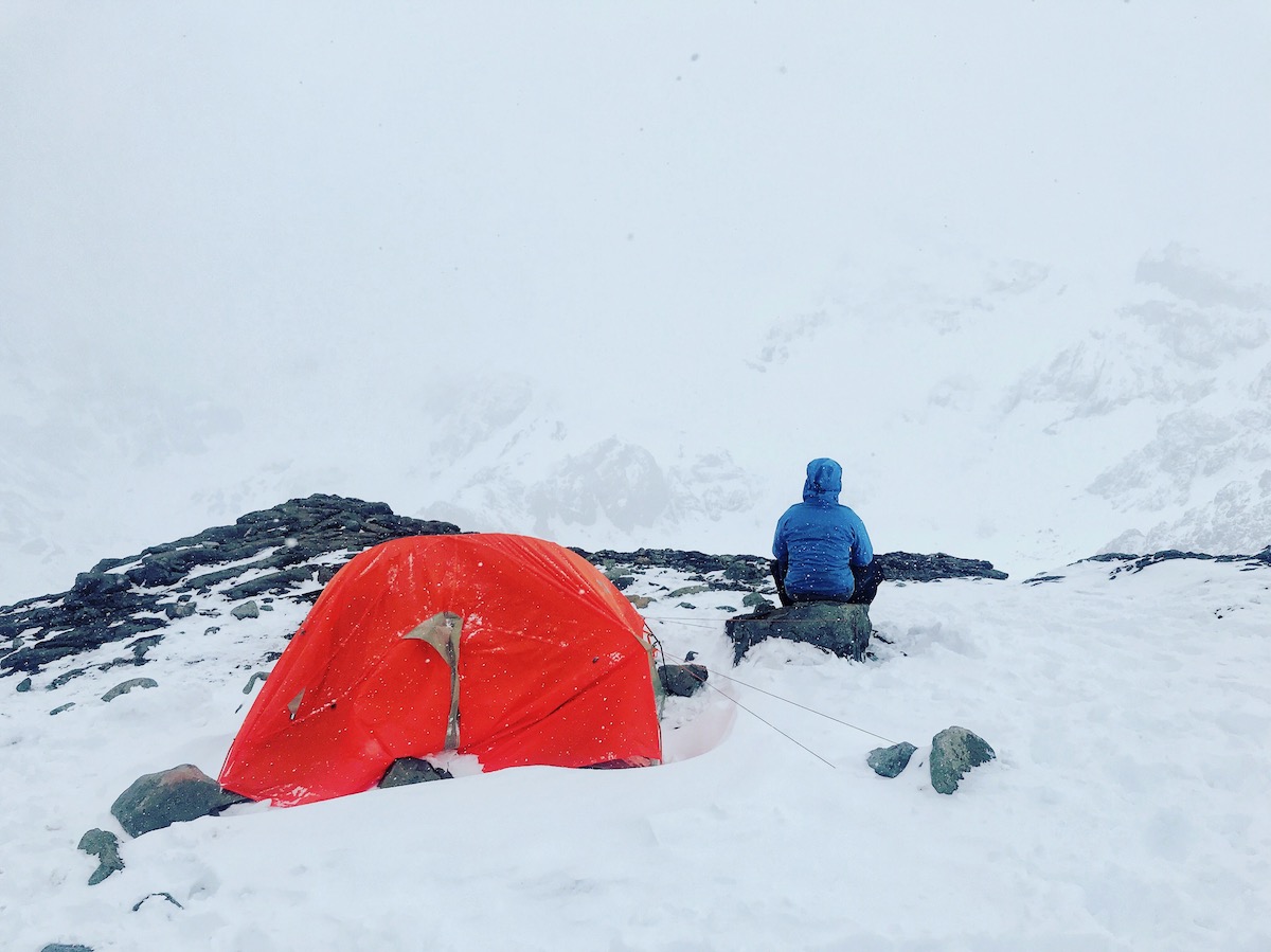 The Only Road Trip Packing List You'll Ever Need! | cold weather travel A solitary man in blue looks out into the wilderness in a snowy harsh climate, next to an orange tent