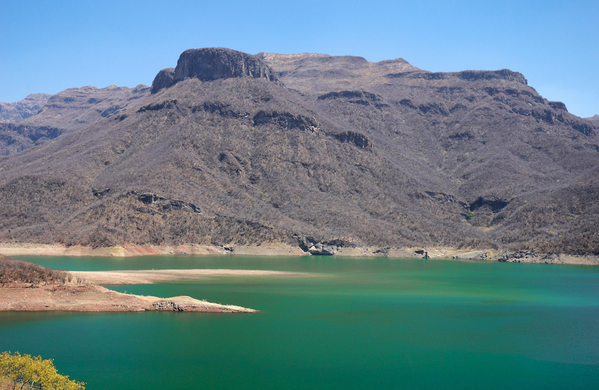 16 Famous Landmarks in Mexico (& How To See Them in 2024!) | copper canyon A copper-coloured mountain overlooks turquoise water.