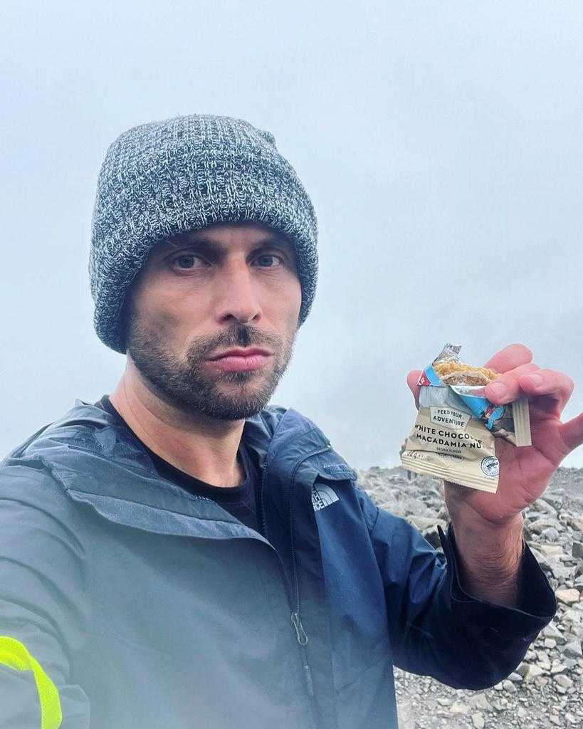 Hiking The UK National 3 Peaks in 24 Hours: An Honest Guide | food gear 3 peaks challenge Hiker eating a Clif bar wearing a hat