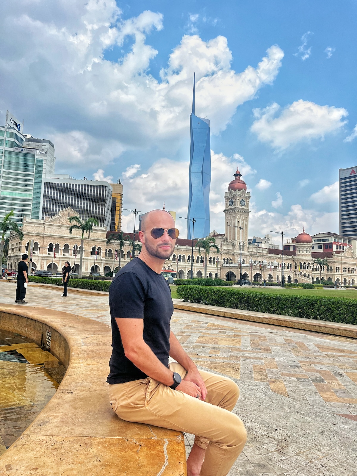 How Many Days Should You Spend in Kuala Lumpur? | how many days kl A male tourist in sunglasses poses in front of a striking government building and modern architecture in Kuala Lumpur, Malaysia