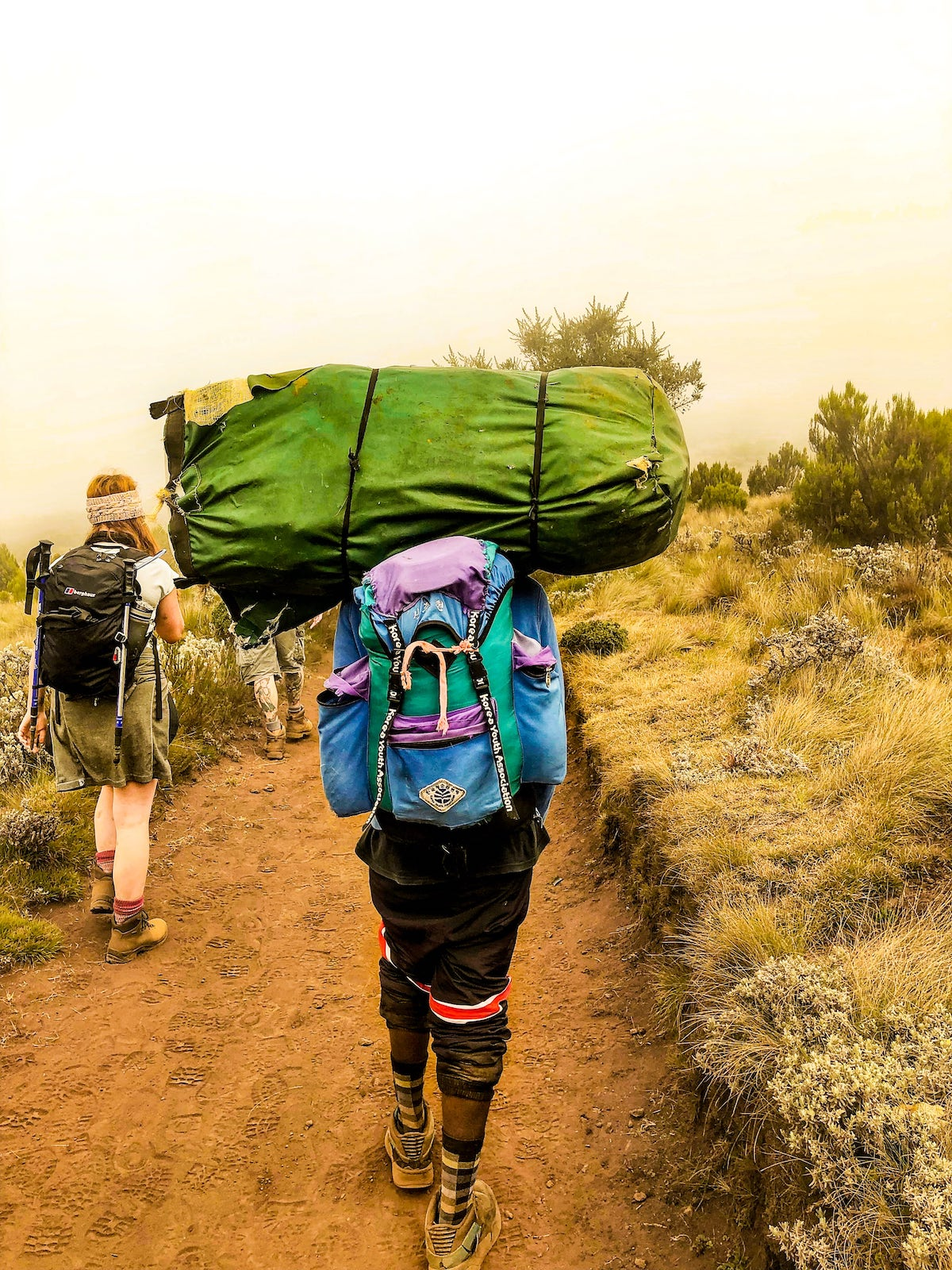 The Beginner's Guide To Climbing Mount Kilimanjaro | image 5 A porter on a mountain carries a large green bag on his head.