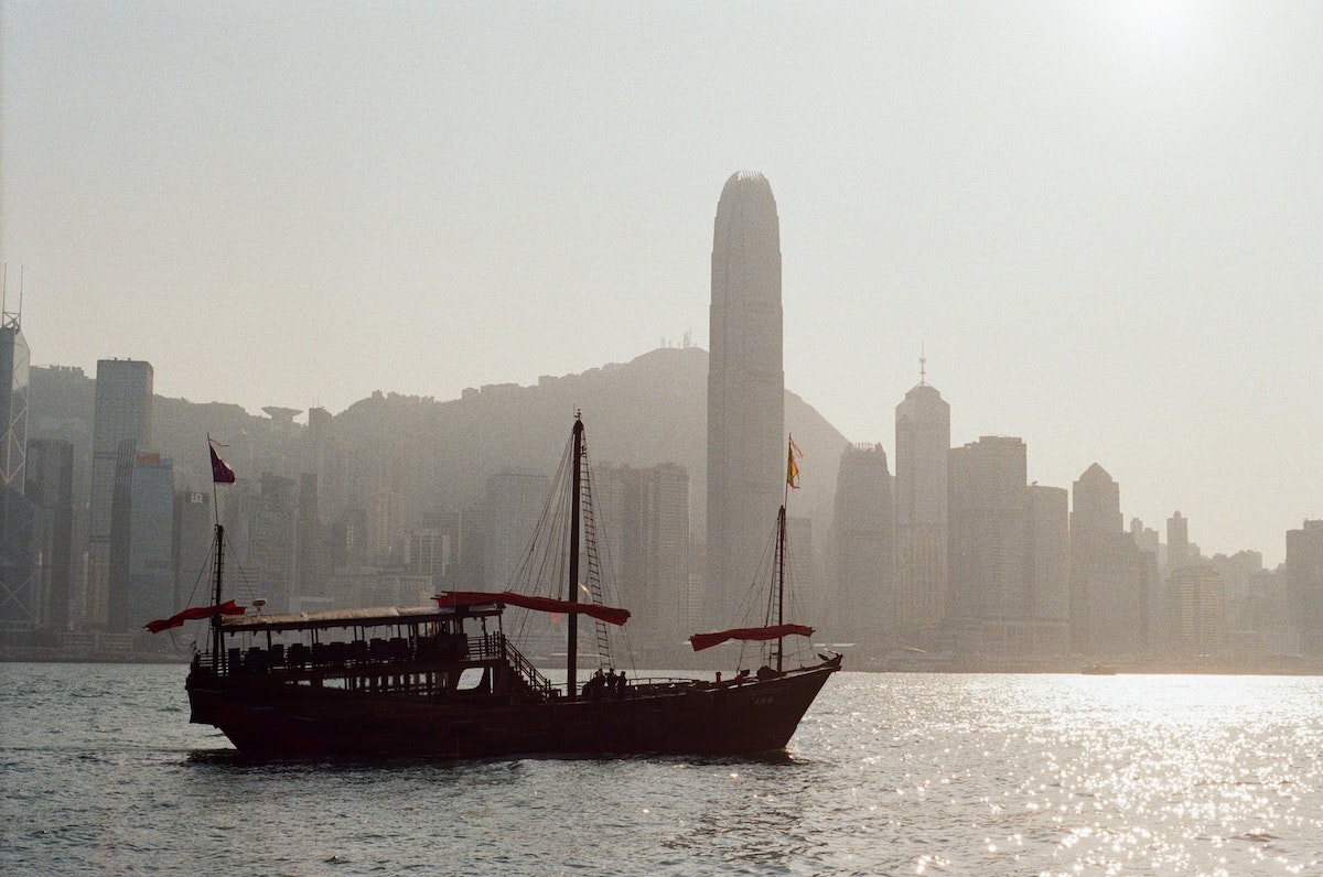 The Ultimate Hong Kong Bucket List: 25 Best Things To Do! | junk boat hong kong A large traditional ship sails across a harbour with skyscrapers in Hong Kong