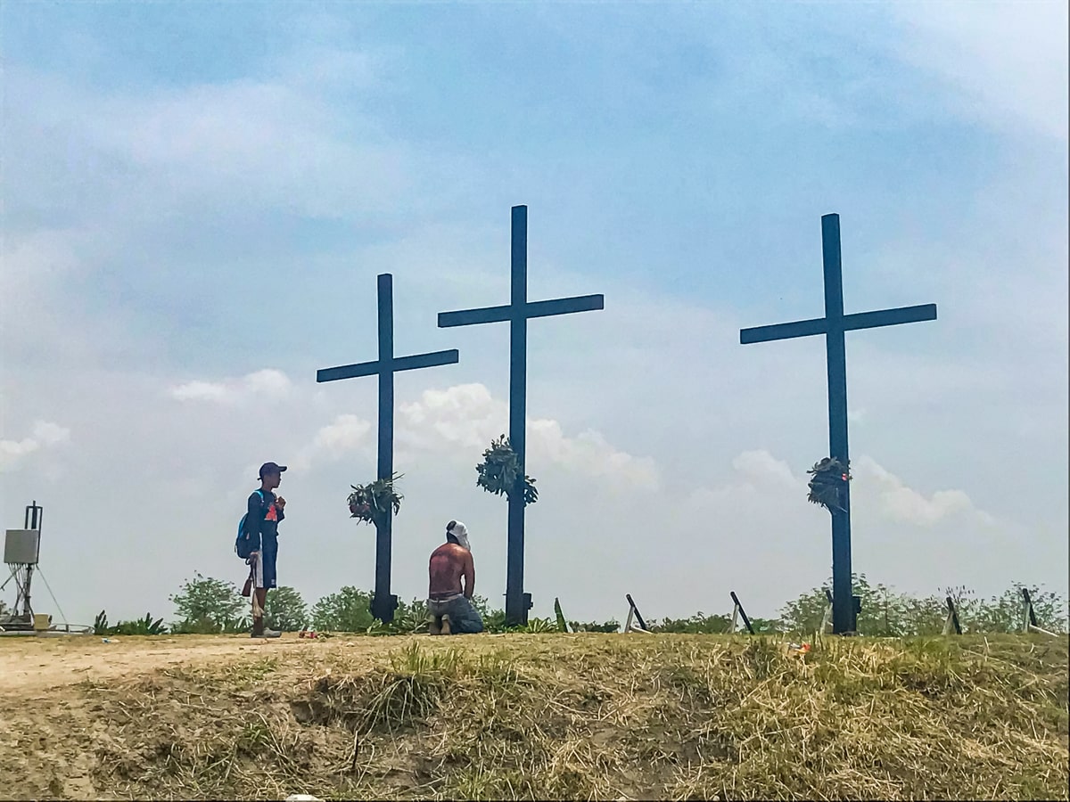 Crucifixion in the Philippines: My (Extreme) Easter Experience | kneeling at cross Philippines A shirtless man kneels in front of three raised crucifixes in The Philippines