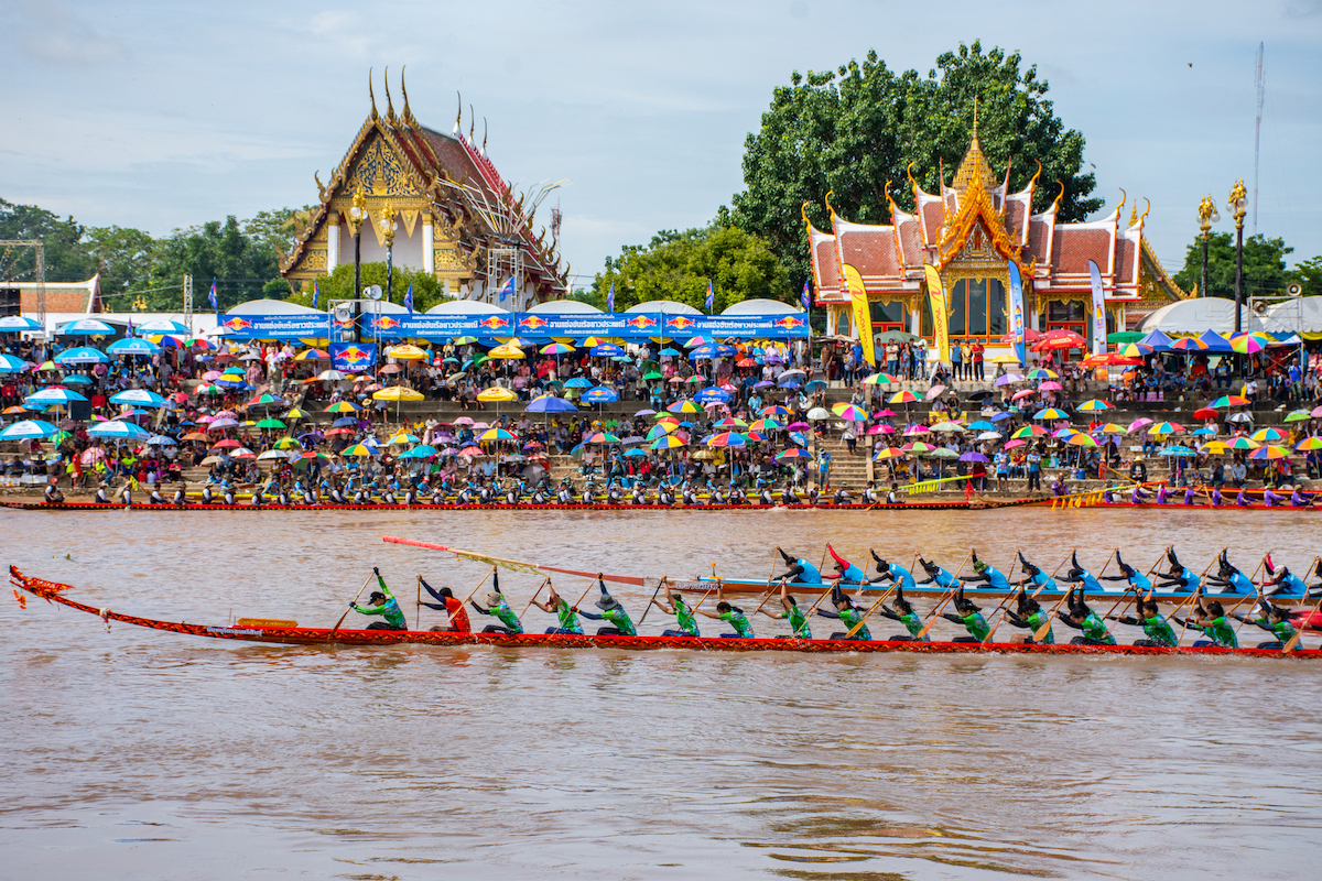 17 Best Thailand Festivals (That You May Never Heard Of) | long boat racing festival thailand Two long boat teams race against each other in a famous Thailand festival with a packed crowd watching in front of two golden temples.