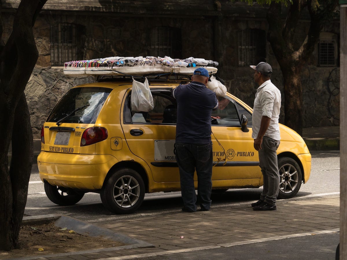 Public Transport in Medellin, Colombia: How To Get Around | medellin Taxi driver arranging sunglasses shades display board on car cab roof in Medellin Antioquia Colombia in South America