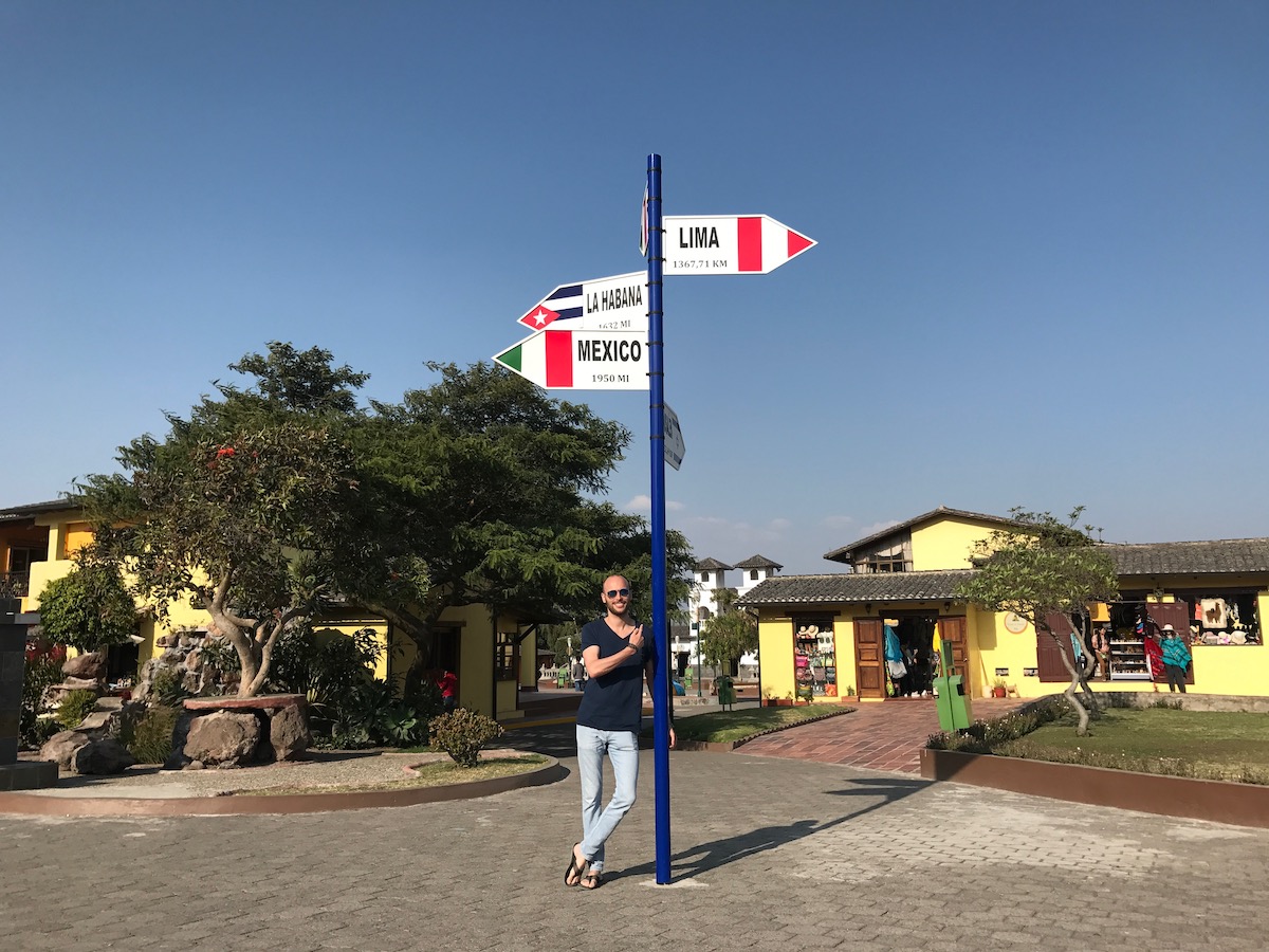 One Week in Quito, Ecuador: 23 Things in 7 Days! | mitad del mundo Quito A man smiles under a signpost pointing to Peru, Cuba and Mexico in La Mitad del Mundo in Quito